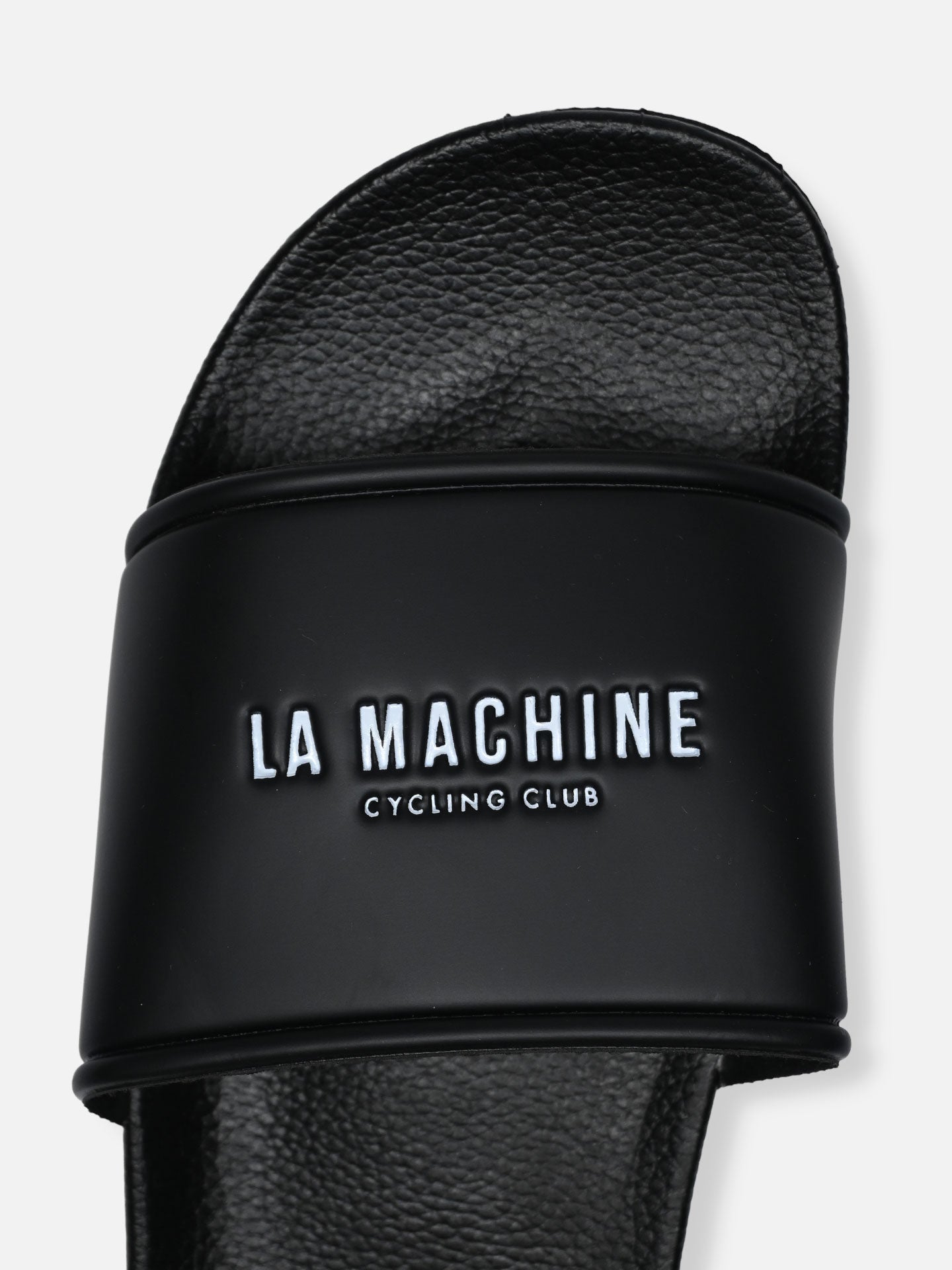 A close-up of La Machine Logo Slides/Slippers by La Machine Cycle Club, featuring LA MACHINE CYCLING CLUB in white on the black strap. These bike slippers have a textured footbed for post-ride comfort and style.