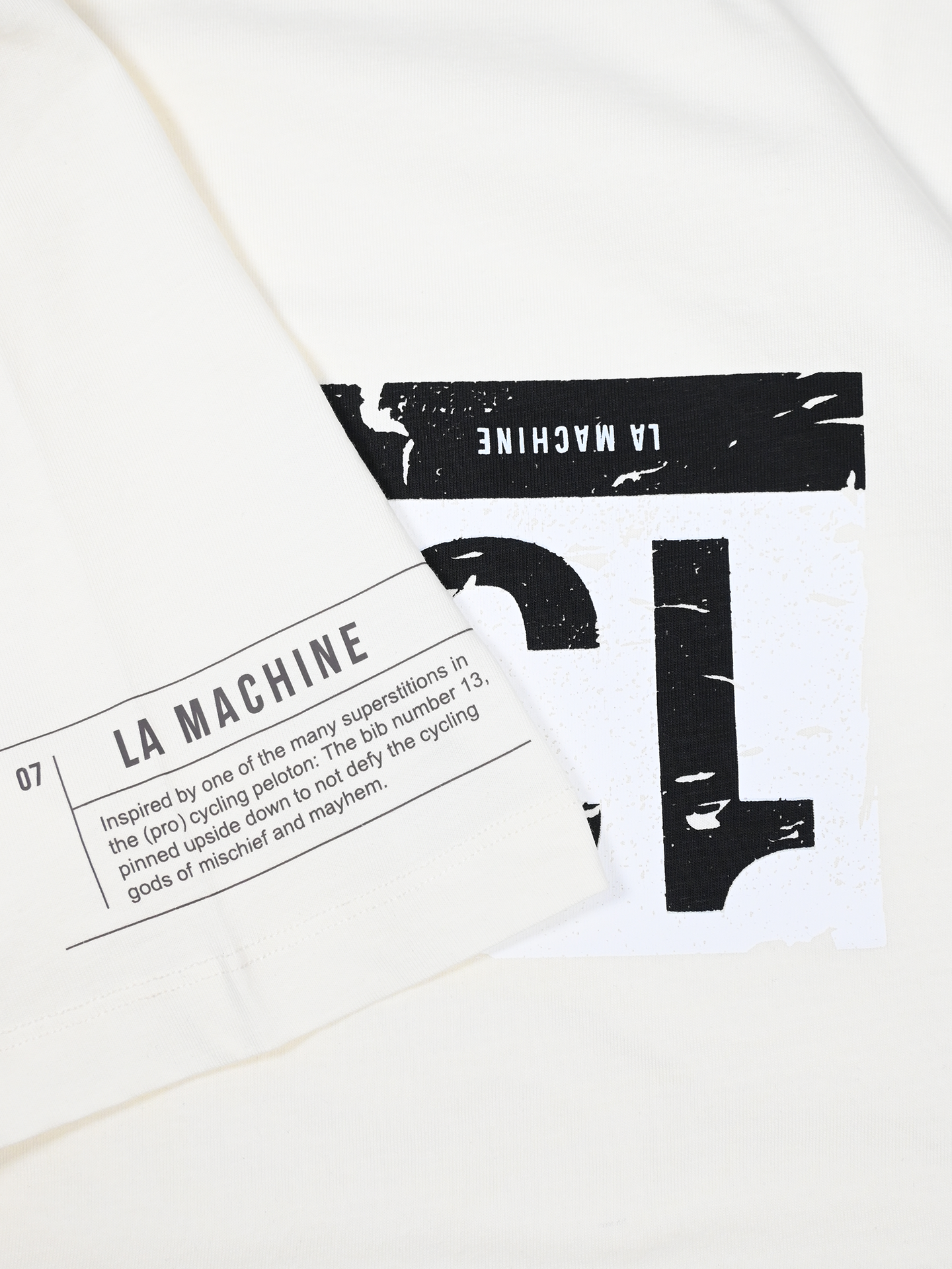 The Bib Number 13 T-shirt by La Machine Cycle Club features two black-and-white patches—one with cycling superstitions—on an off-white unisex cotton tee, perfect for cycling fans.