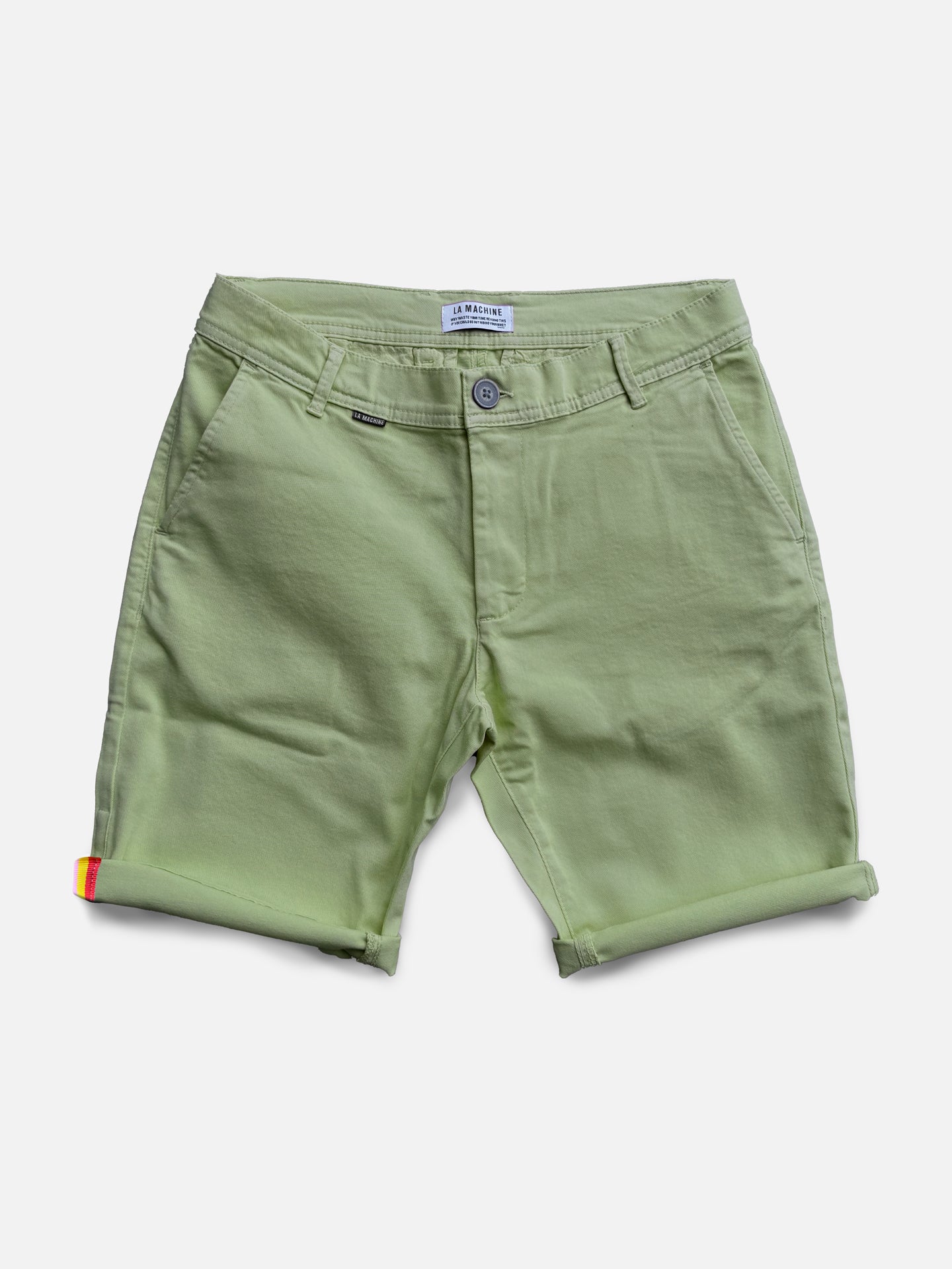 The Grand Tours Rest Day Bermuda in Dusty Green by La Machine Cycle Club features a semi-tailored fit, front/back pockets, belt loops, and button closure. A folded hem with a red-yellow tag adds style—ideal for relaxed days.