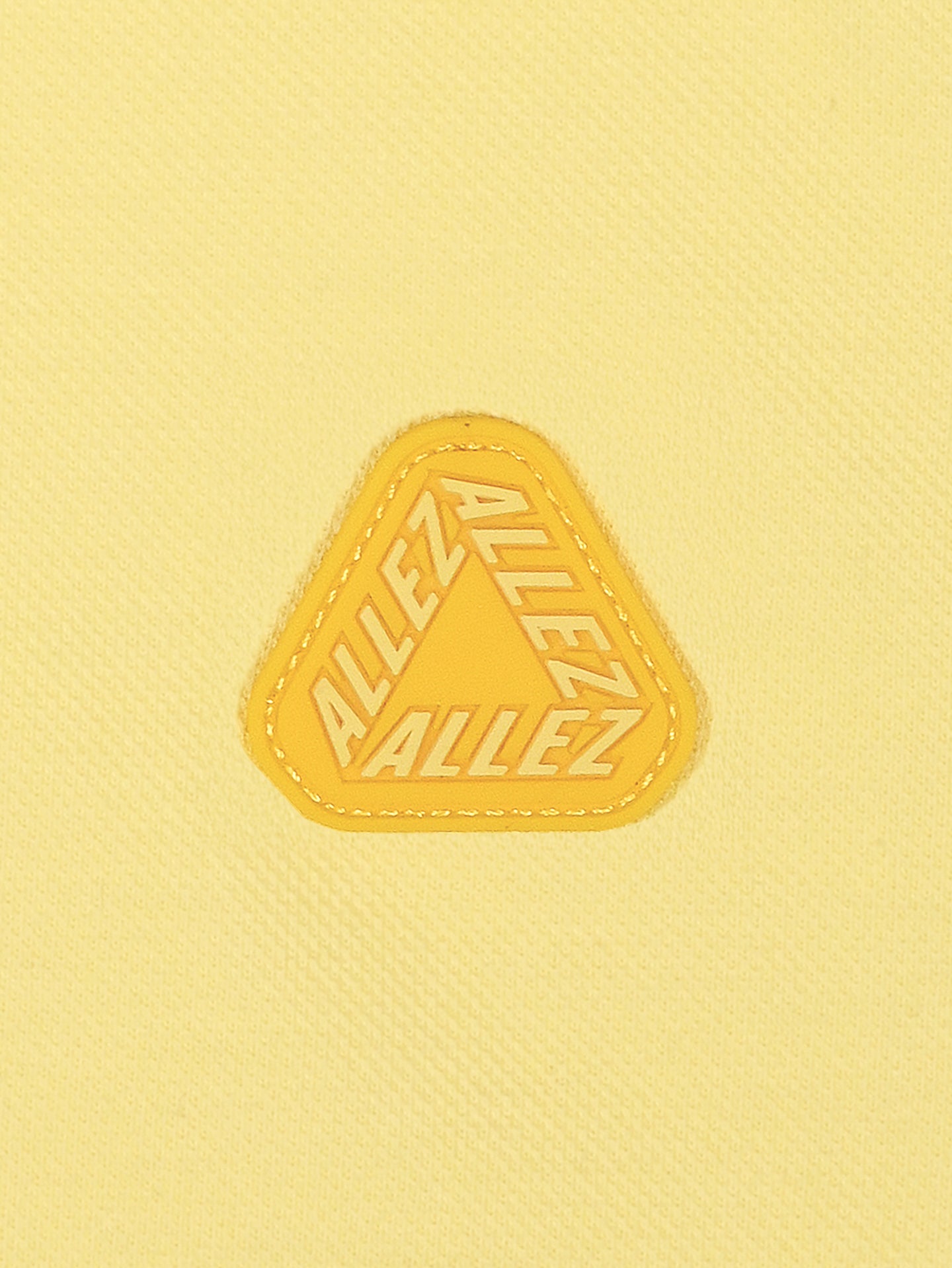 The La Machine Cycle Club Allez - Tour de France Polo Shirt in light yellow features a yellow triangular patch with ALLEZ repeated three times, celebrating the spirit of the Tour de France.