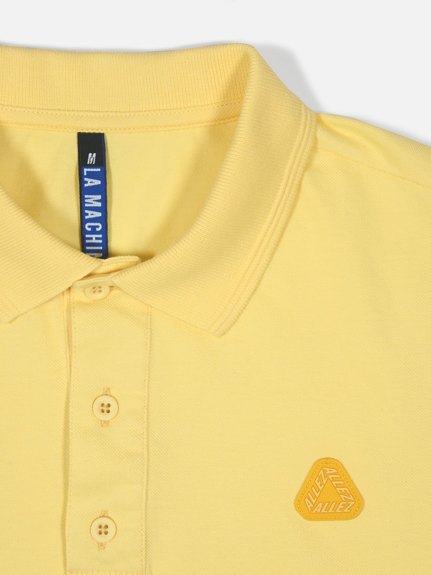 A close-up of the Allez - Tour de France Polo Shirt in light yellow by La Machine Cycle Club, featuring a collar, three buttons, and a small embroidered “ALLEZ” badge near the chest. Inspired by classic Tour de France polo shirts.