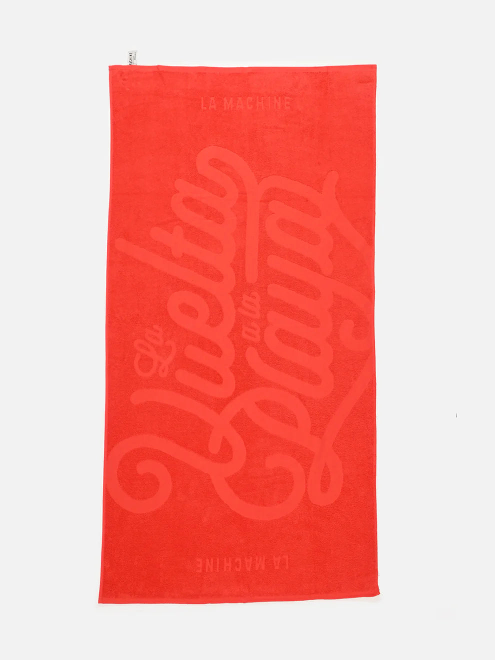 A vibrant red 100% cotton beach towel from La Machine Cycle Club’s Grand Tours - Towel Bundle, featuring large woven “La Vuelta a la Playa” text and smaller “La Machine” details above and below.