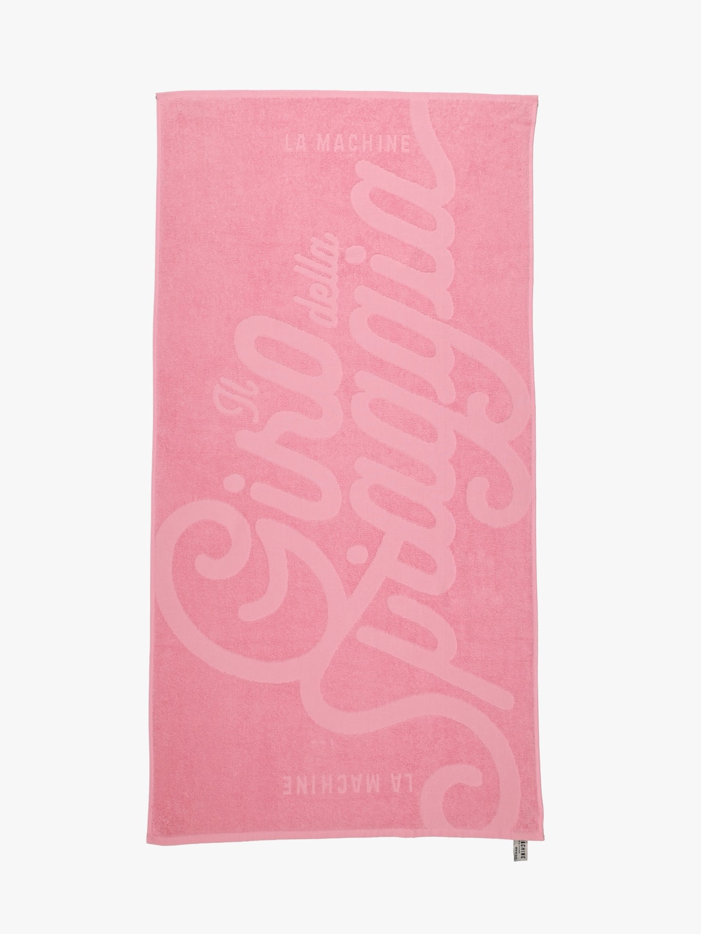 The Il Giro della Spiaggia - Beach Towel by La Machine Cycle Club is a rectangular pink towel featuring bold, italic Il giro della spiaggia text with smaller La Machine at the top and bottom, inspired by Grand Tour style.