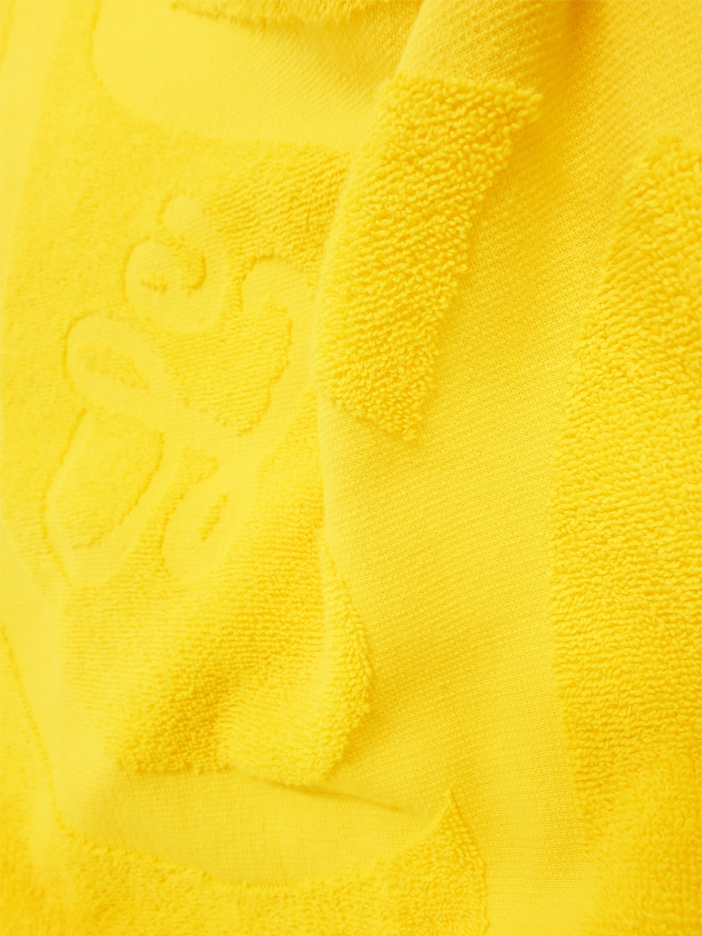Close-up of the Le Tour de la Plage Beach Towel by La Machine Cycle Club, showing its yellow textured fabric with an embossed bee and honeycomb design. The towel looks soft, absorbent, and ideal for cycling enthusiasts.