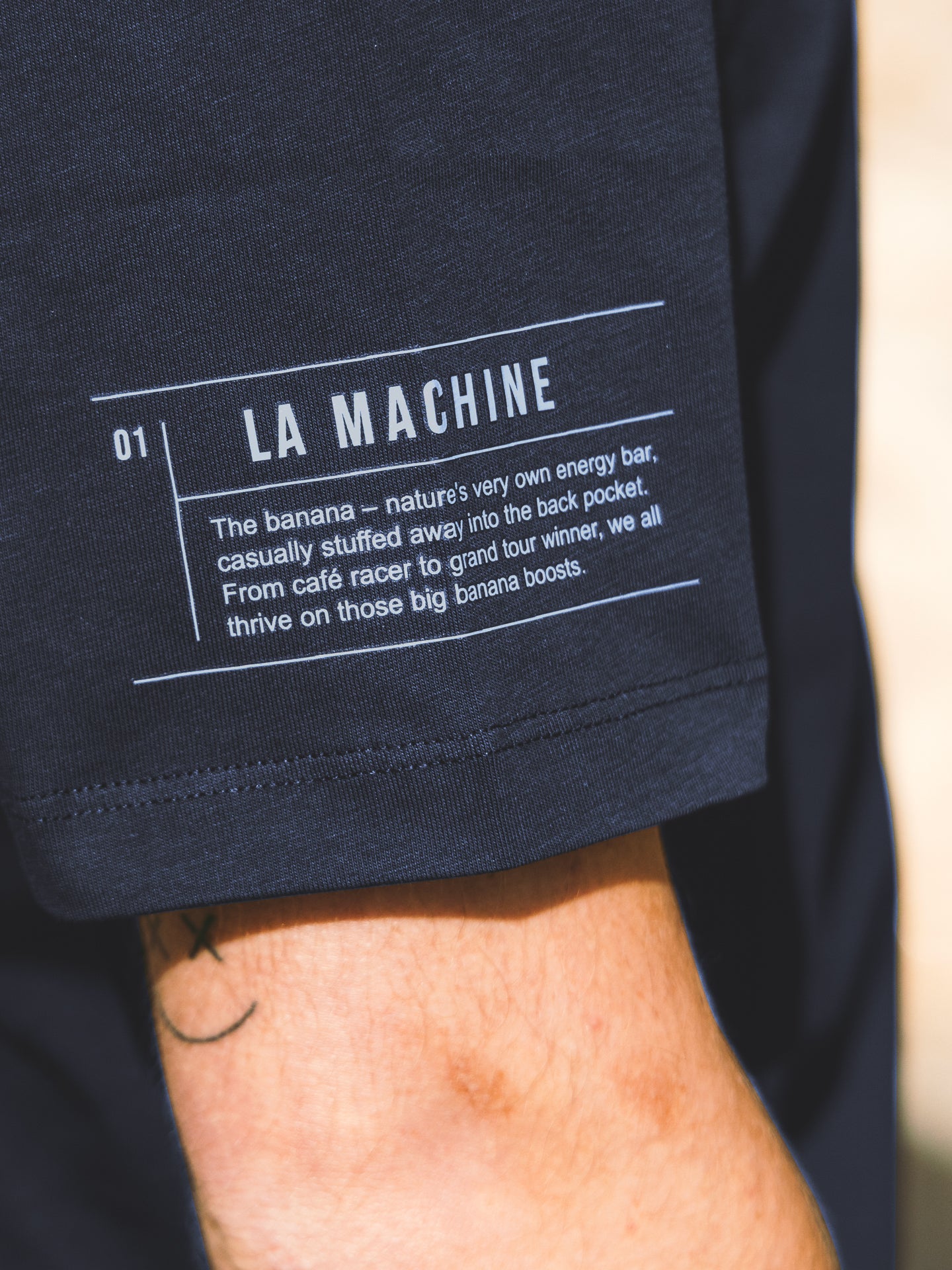 Close-up of the In the Pocket mens navy T-shirt by La Machine Cycle Club, showing its sleeve with a white LA MACHINE label—celebrating the banana pocket for handy, natural energy on every ride.