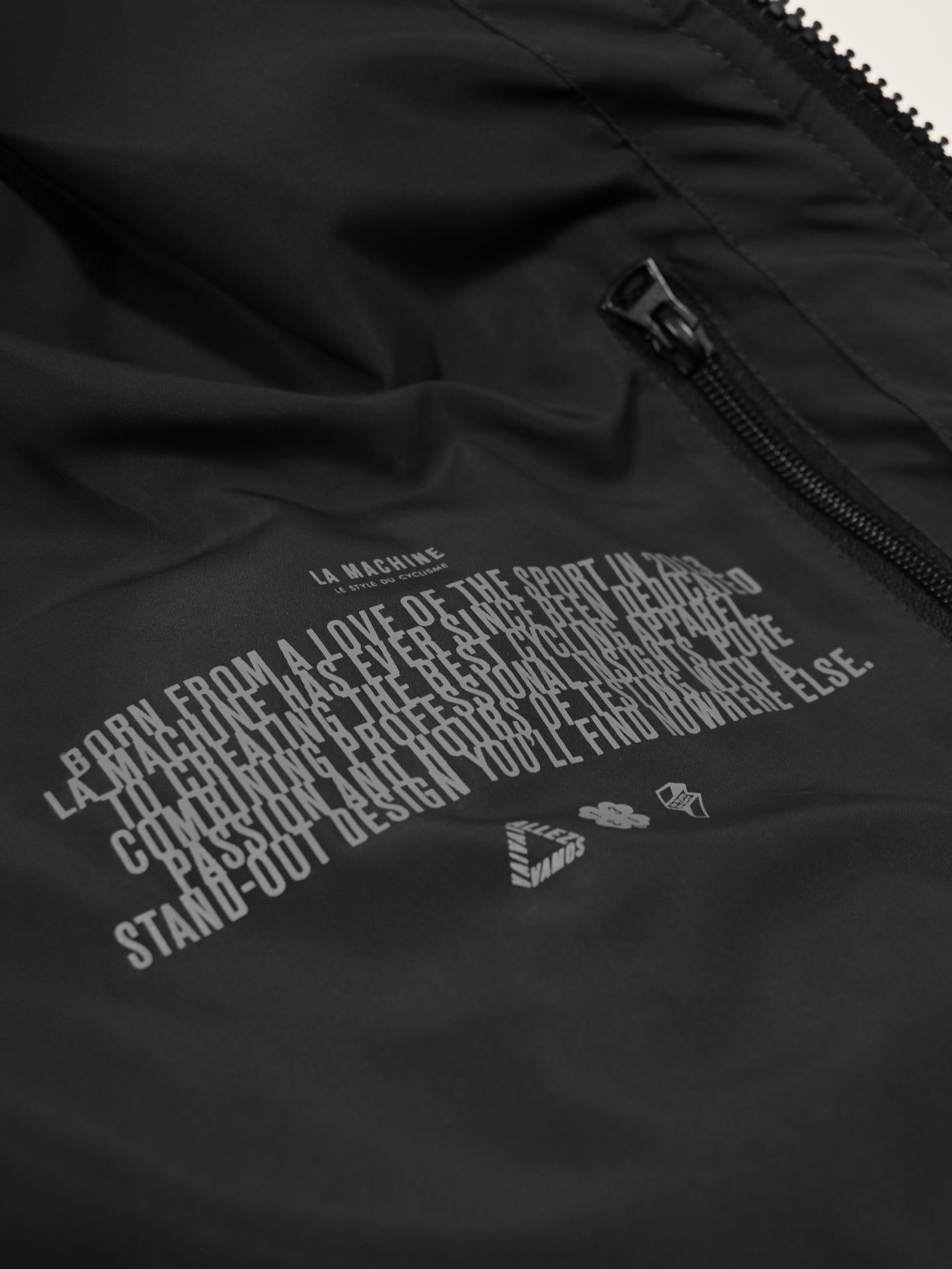 Close-up of the inside of the Beyond the bike - Padded Jacket in black by La Machine Cycle Club, featuring a zippered pocket, printed brand story and design philosophy, plus graphic icons below the text.