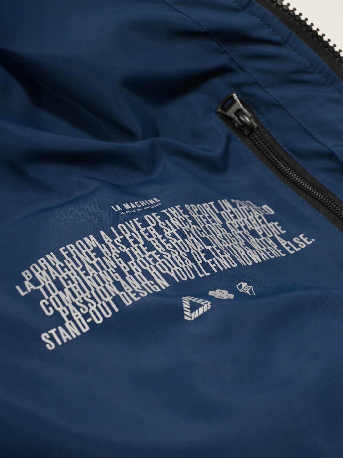 Close-up of a navy blue Beyond the bike padded jacket’s inner lining by La Machine Cycle Club, featuring white printed text, zipper detail, and part of a pocket; the text highlights the jacket’s inspiration and unique design.