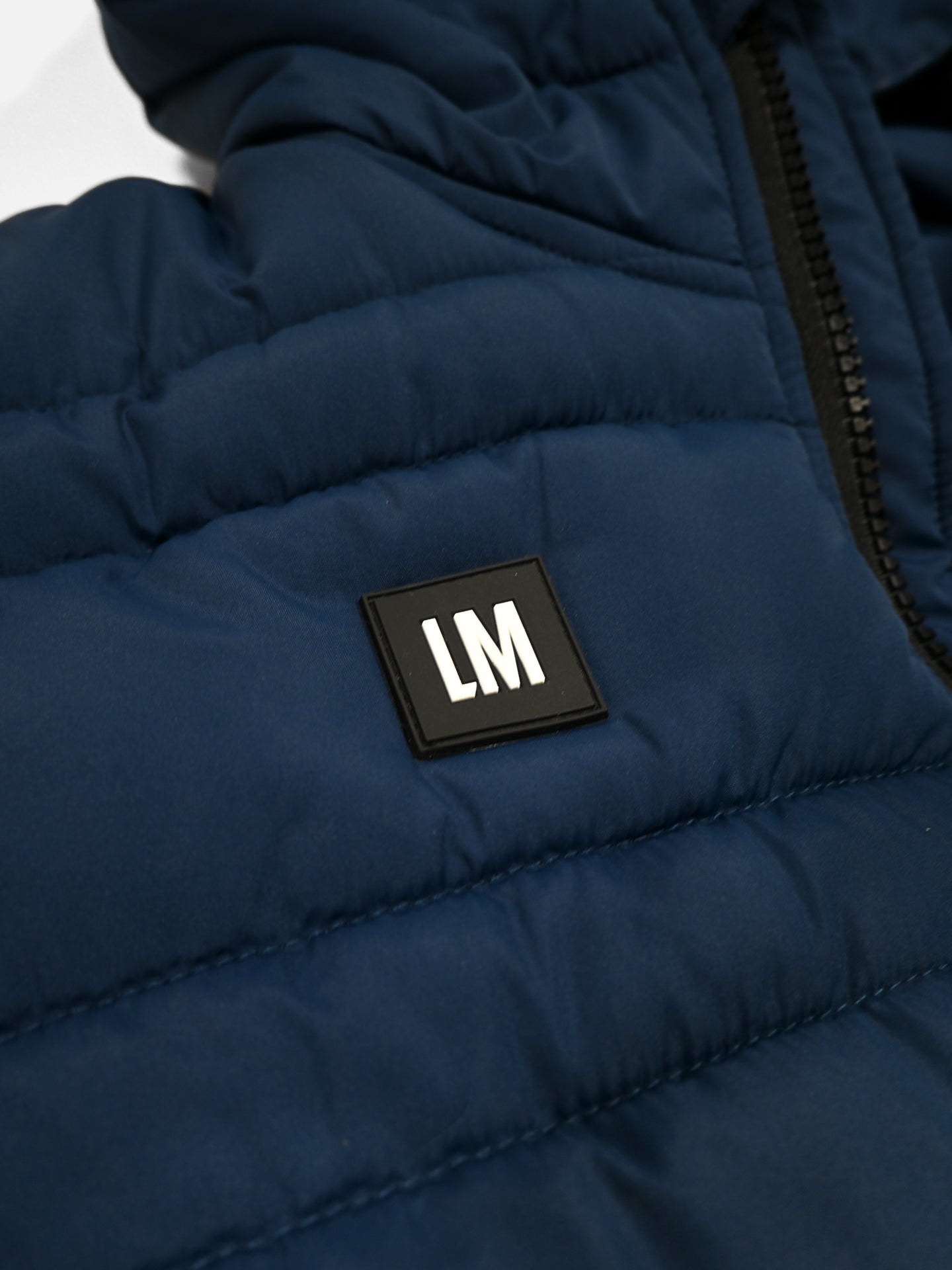 A close-up of the Beyond the bike - Padded Jacket - Blue by La Machine Cycle Club, a unisex navy jacket featuring a chest patch with “LM” near the black zipper.