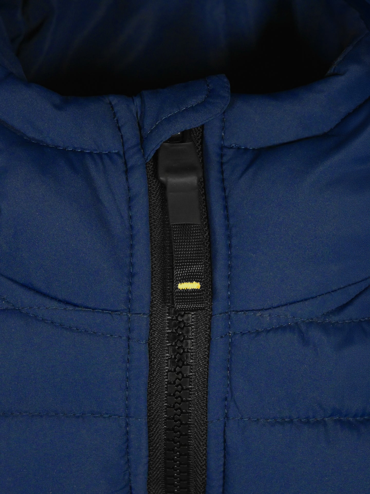Close-up of the La Machine Cycle Club Beyond the Bike Padded Jacket in blue, showing a black zipper with yellow detail. This unisex jacket features visible stitched seams and a cozy, quilted padded texture.