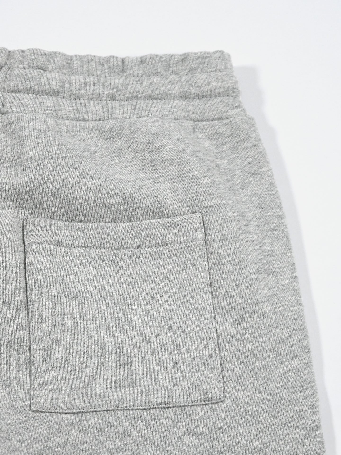 Close-up of La Machine Cycle Clubs Beyond the bike Sweatshorts in Melange Grey, showing textured fabric, a relaxed fit, elastic waistband, and a right-side square back pocket against a plain white background.