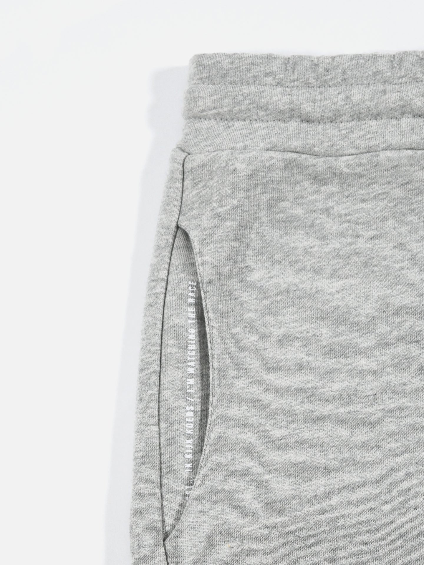 Close-up of Beyond the Bike Sweatshorts in Melange Grey by La Machine Cycle Club, featuring a relaxed fit, elastic waistband, and a side pocket with subtle white printed text inside.