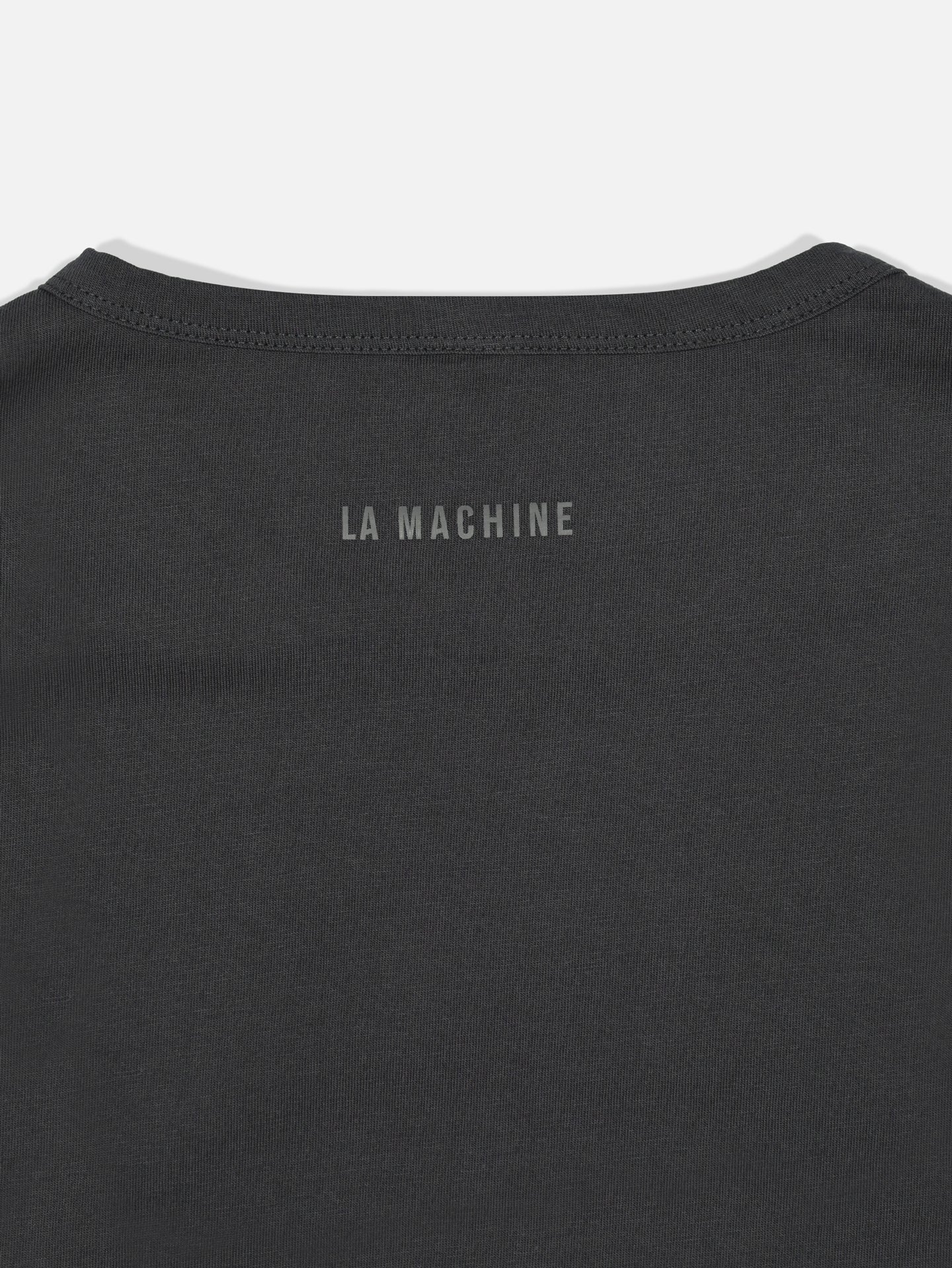 A close-up of the upper back of the Bib Number 13 - T-shirt - Charcoal Teal by La Machine Cycle Club, featuring LA MACHINE printed in simple gray capital letters.