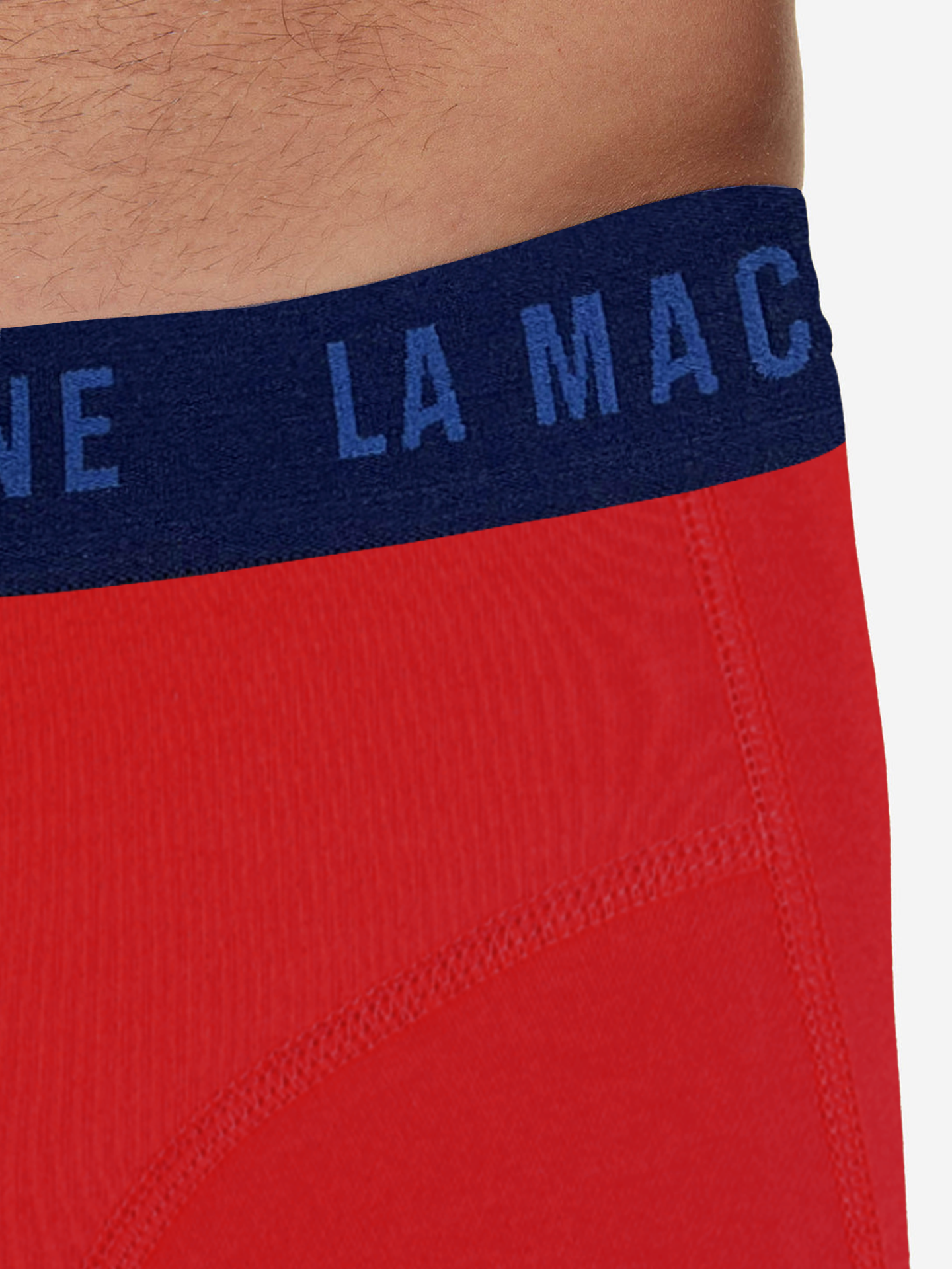 Close-up of a person’s waist wearing La Machine - Boxershorts - Vuelta Red by La Machine Cycle Club, featuring a navy blue elastic waistband with partially visible white text. The plain, light background highlights these stylish men’s boxershorts.