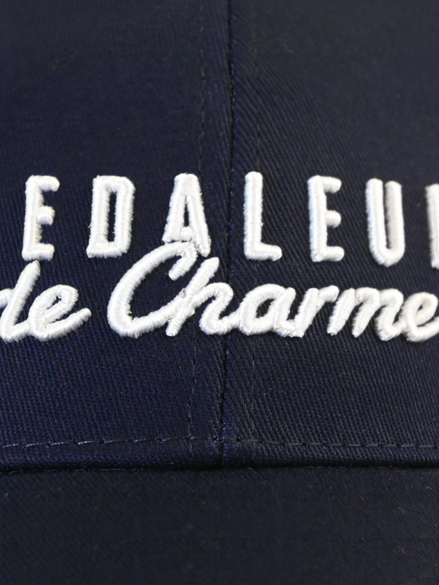 Close-up of navy fabric on the La Machine Cycle Club Pedaleur de Charme - Casual Cap, a 6-panel cap featuring white embroidered EDALEU and le Charme text in cursive and block letters.