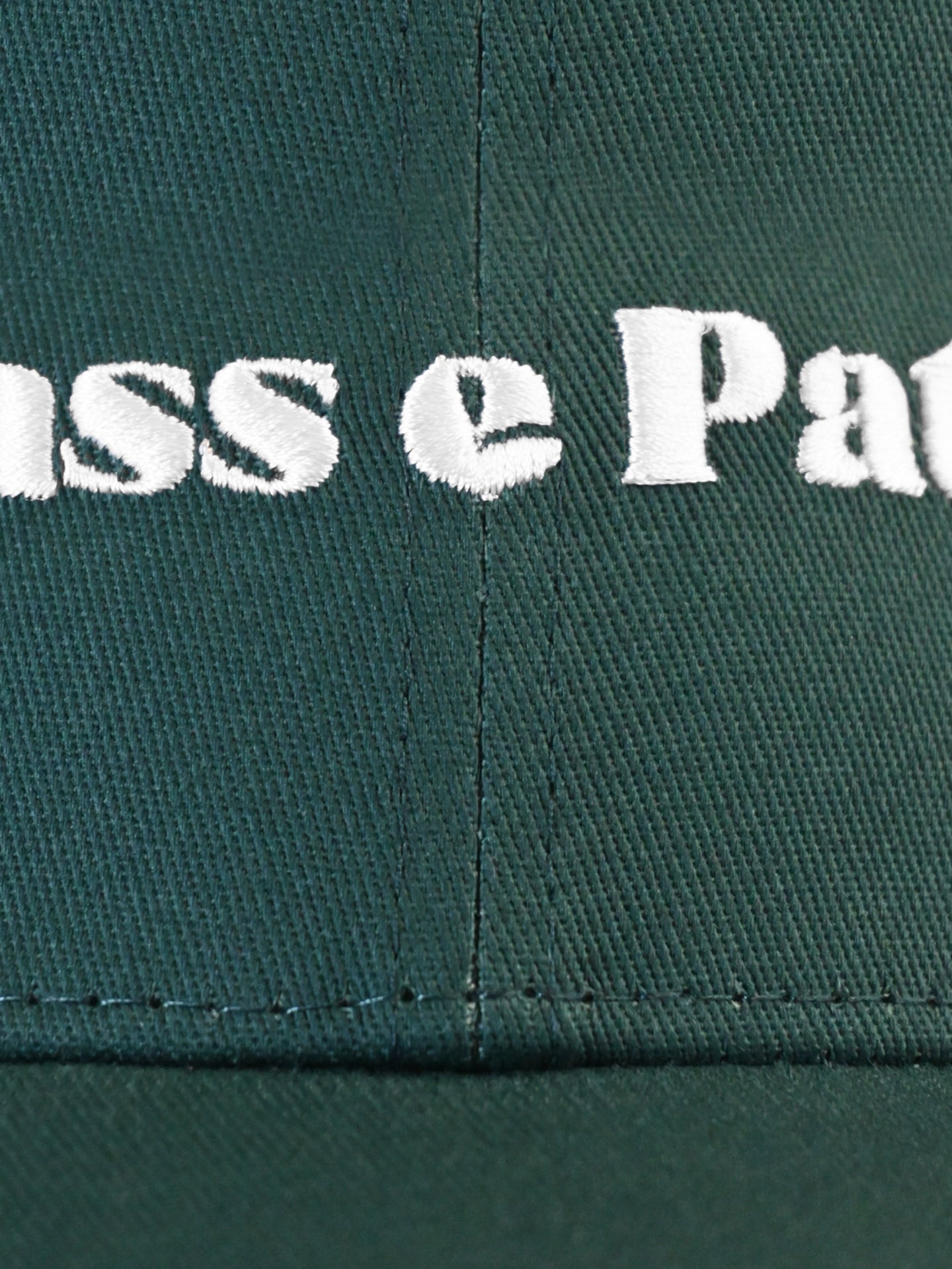 Close-up of green fabric from the La Machine Cycle Club Chasse Patate - Casual Cap, featuring detailed white embroidered text and showcasing the caps fine stitching and texture.