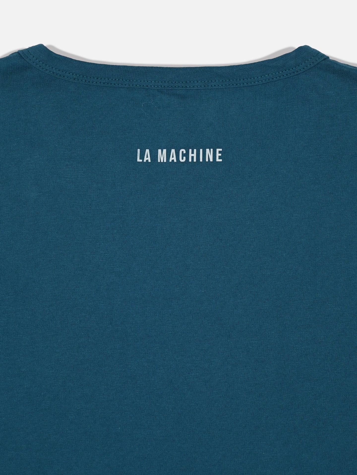 A close-up of the back neckline of a blue Coffee Ride Winners Club T-shirt by La Machine Cycle Club, featuring LA MACHINE printed in white below the collar—ideal for your next coffee ride or cycling adventure.
