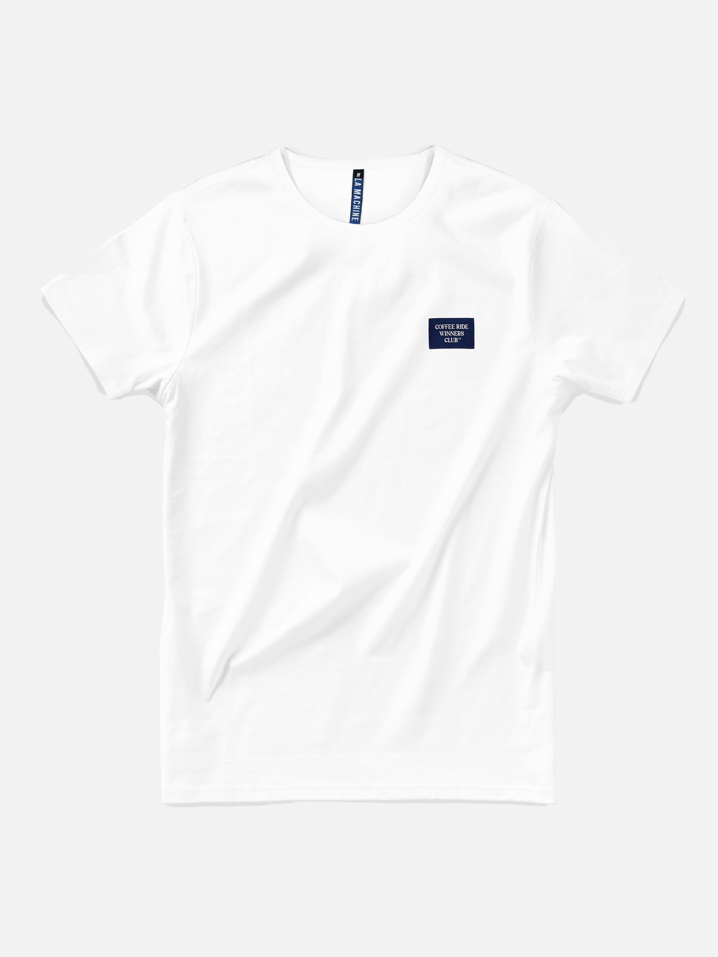 The La Machine Cycle Club Coffee Ride Winners Club T-shirt in white is a unisex tee with a small navy blue rectangular patch and white text on the left chest—ideal for your next coffee ride, shown laid flat on a light background.