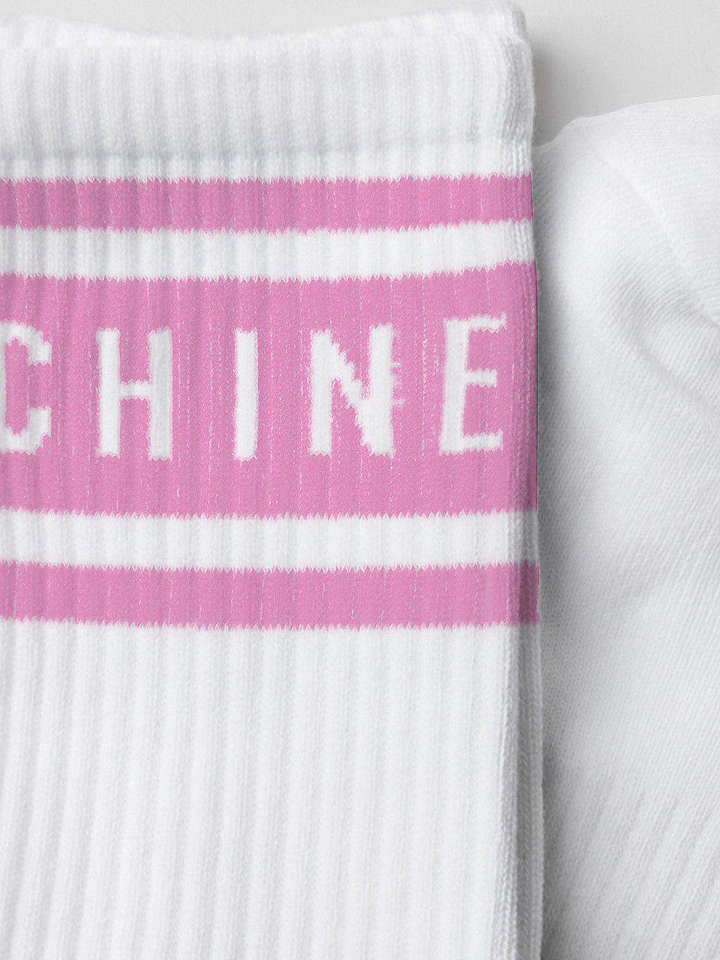 Close-up of the La Machine Cycle Clubs Crew Socks in Giro Pink, showing a white ribbed sock with a pink band near the top and “CHINE” lettering. Another white cycling sock is partially visible beside it.
