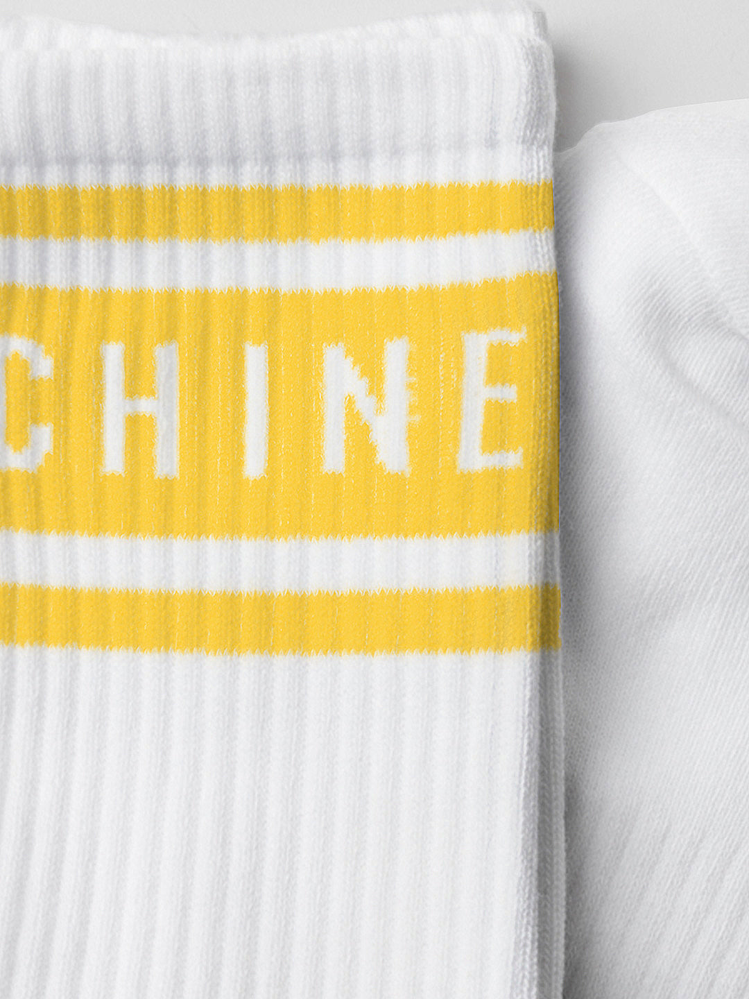 A close-up of La Machine Cycle Clubs La Machine - Crew Socks - Tour Yellow, featuring white ribbed fabric with Le Tour-yellow stripes and white CHINE lettering across the bands.