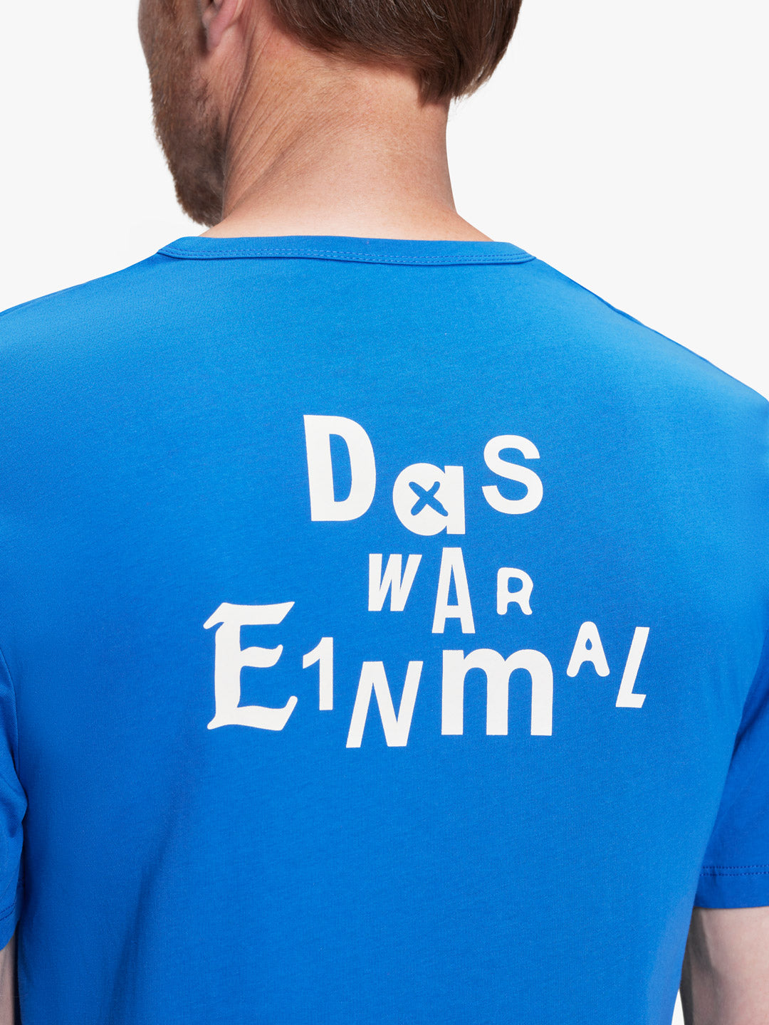 A man models the La Machine Cycle Club De Rode Lantaarn - Das War Einmal unisex blue t-shirt, featuring “Das war einmal” in white fonts on the back—a subtle homage to cycling podcast De Rode Lantaarn.