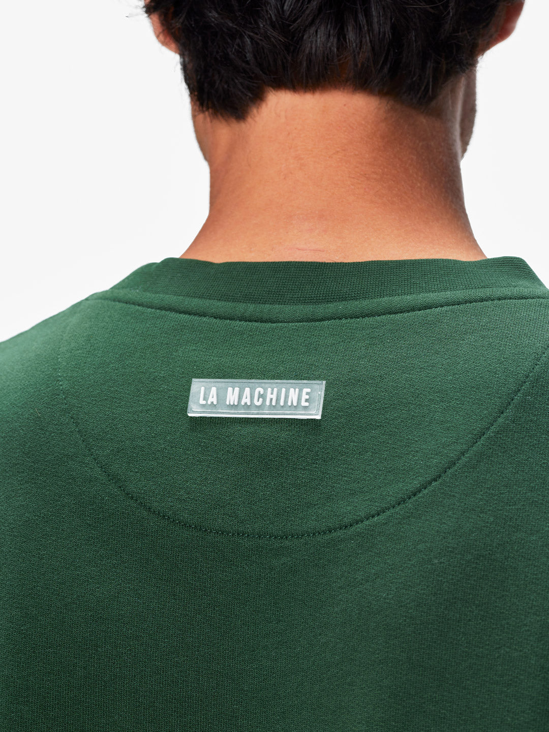 A person is seen from behind wearing the Domestique - Sweatshirt, a green mens loose fit piece by La Machine Cycle Club, featuring the LA MACHINE label sewn just below the neckline on the upper back.