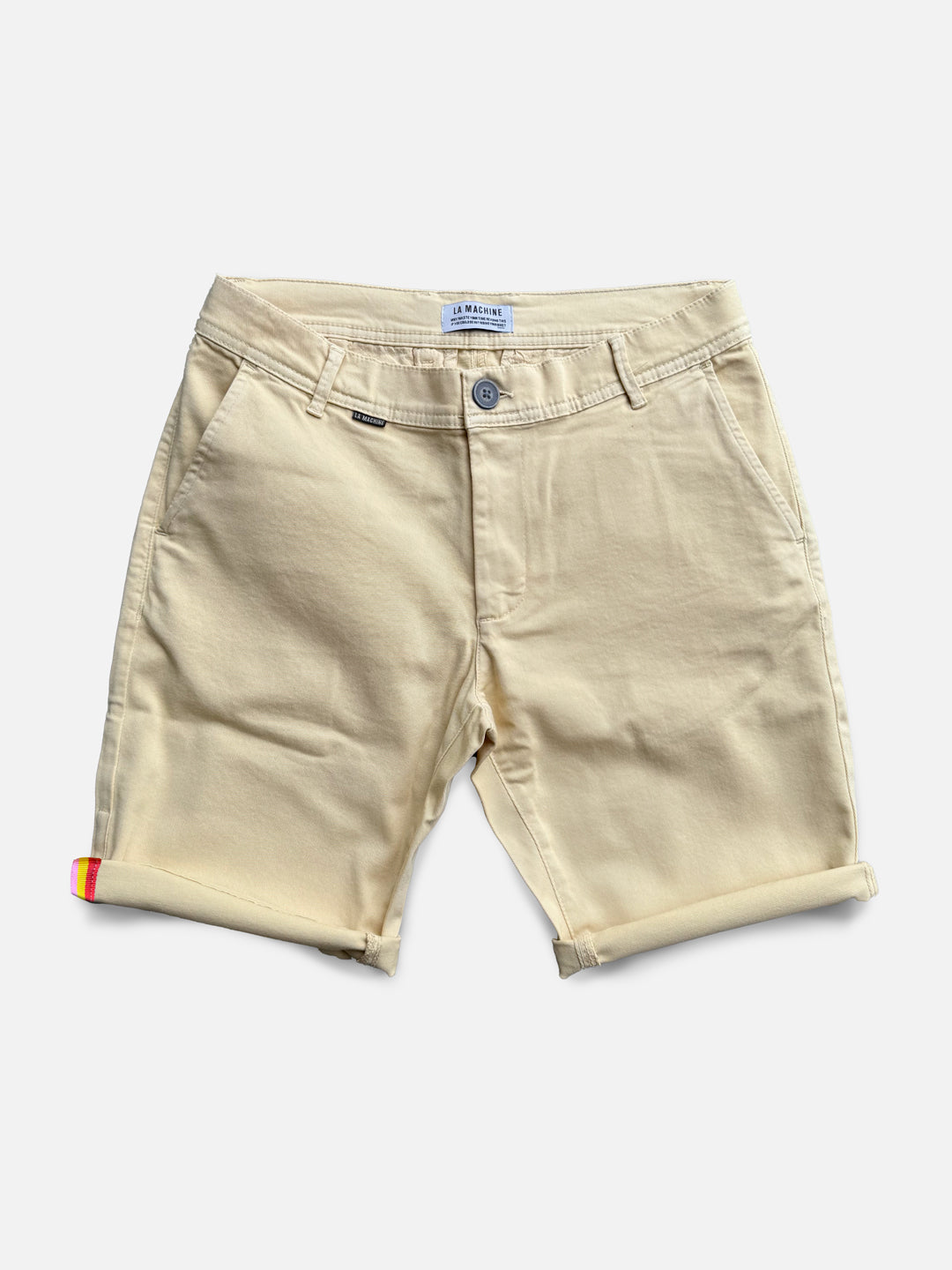 The Grand Tours - Rest Day Bermuda in sand by La Machine Cycle Club is a beige, semi-tailored men’s short with rolled cuffs, front/back pockets, button-zip closure, and a colored tape detail on the left cuff. Displayed flat on white background.