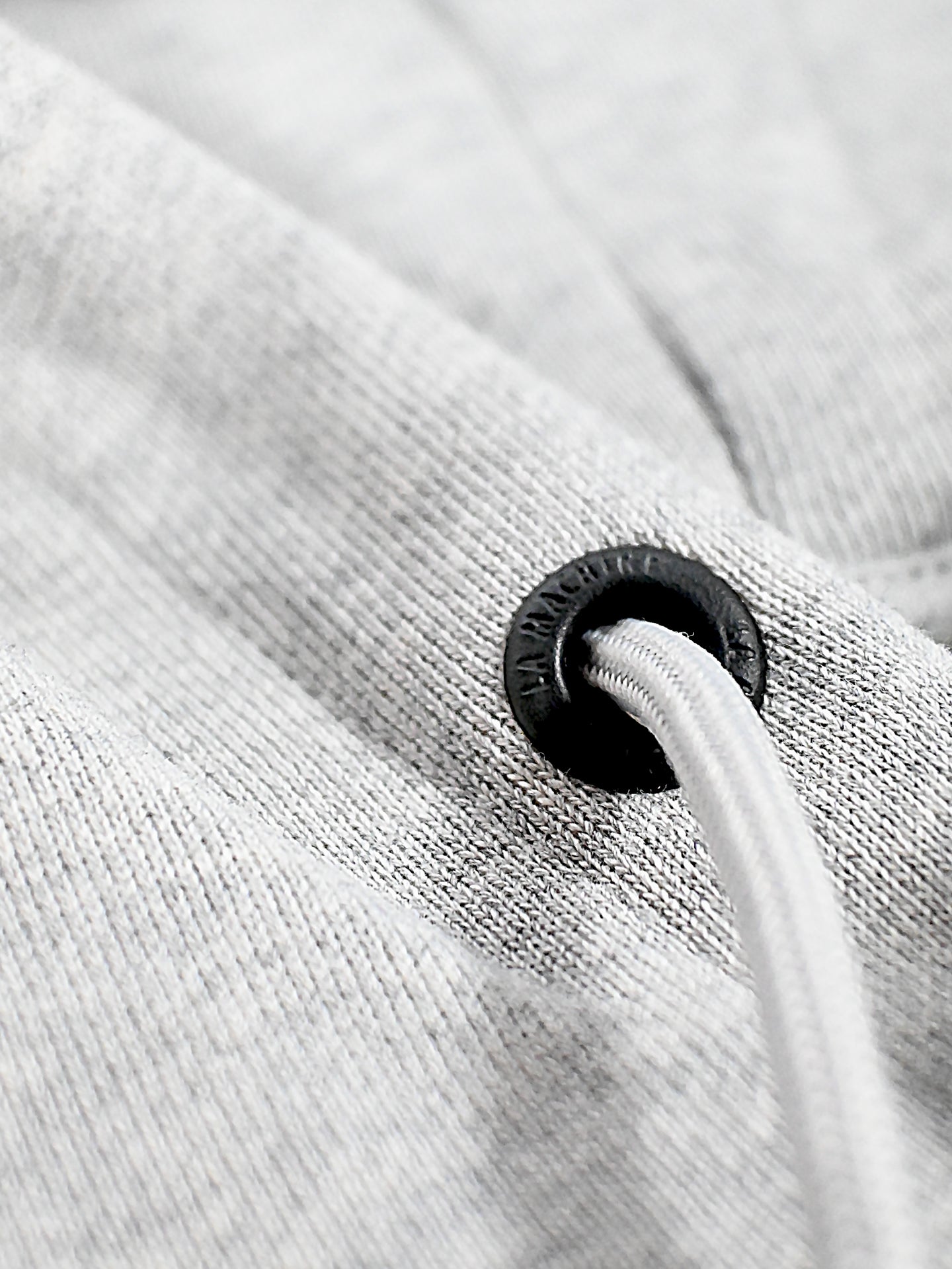 Close-up of a white drawstring threaded through a black metal eyelet on light grey fabric, showcasing the texture and stitching quality of the LMCC - University Hoodie by La Machine Cycle Club.