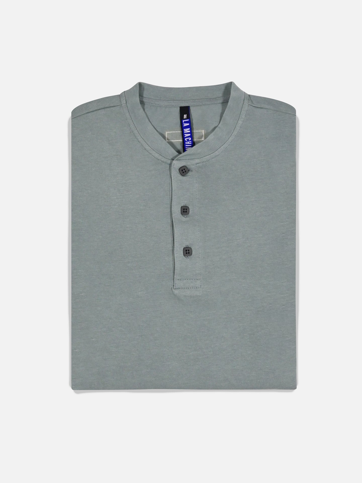 A neatly folded Roubaix Blue Le Pavé Henley long sleeve T-shirt by La Machine Cycle Club, featuring three buttons and a visible blue tag, displayed on a plain white background.