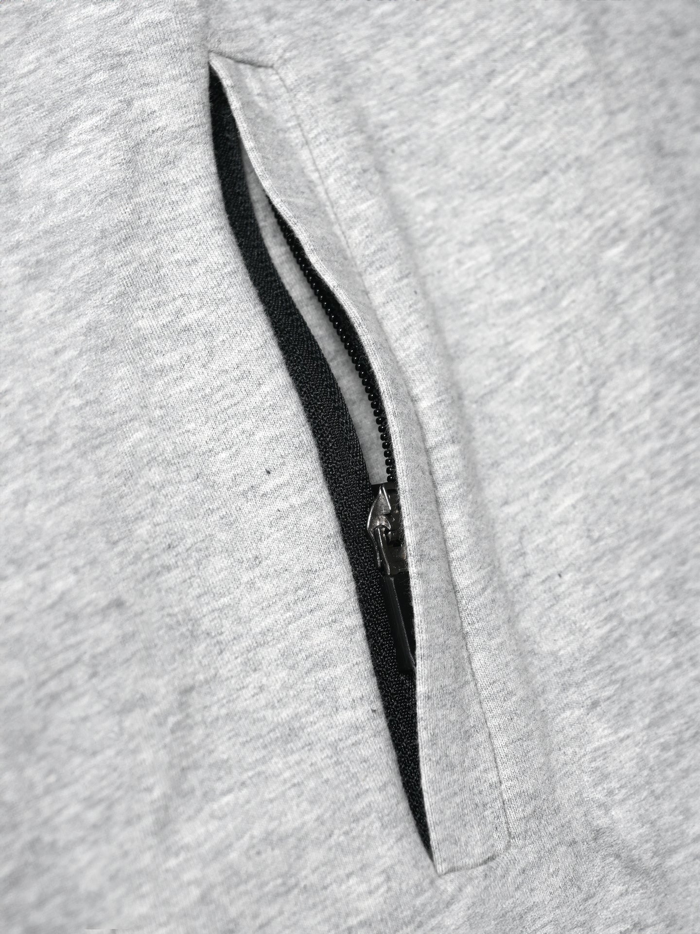 Close-up of a partially unzipped black zipper on light grey fabric from the Lucky 13 Zipped Hoodie by La Machine Cycle Club.