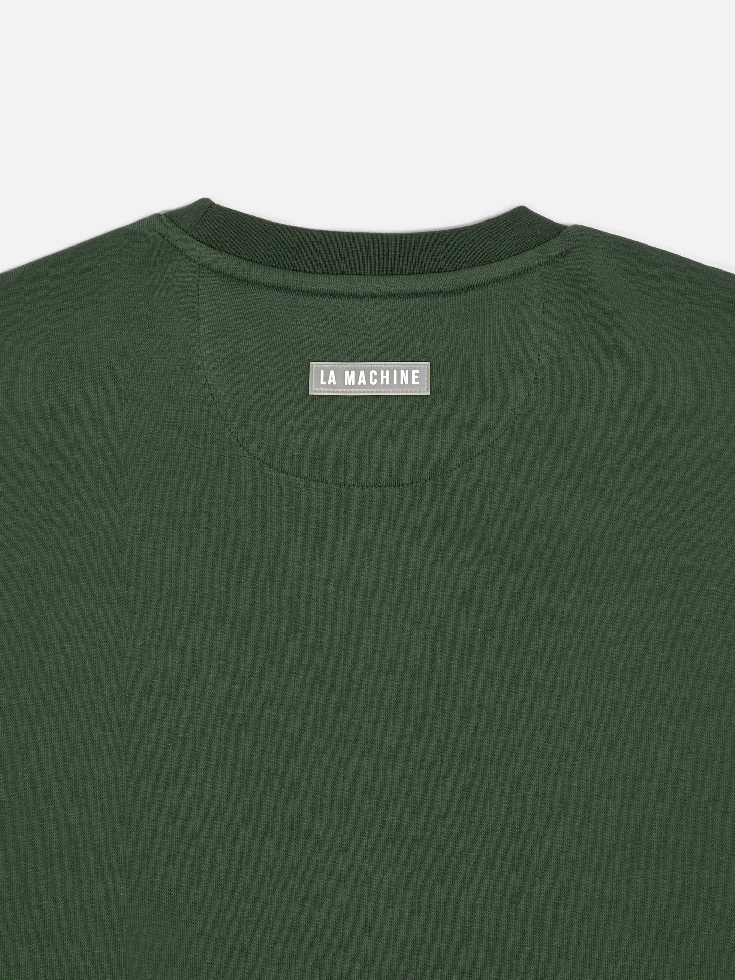 A close-up of the back neck area of the Maillot Vert - Sweatshirt by La Machine Cycle Club, made in EU, featuring a gray fabric label with LA MACHINE in white letters.
