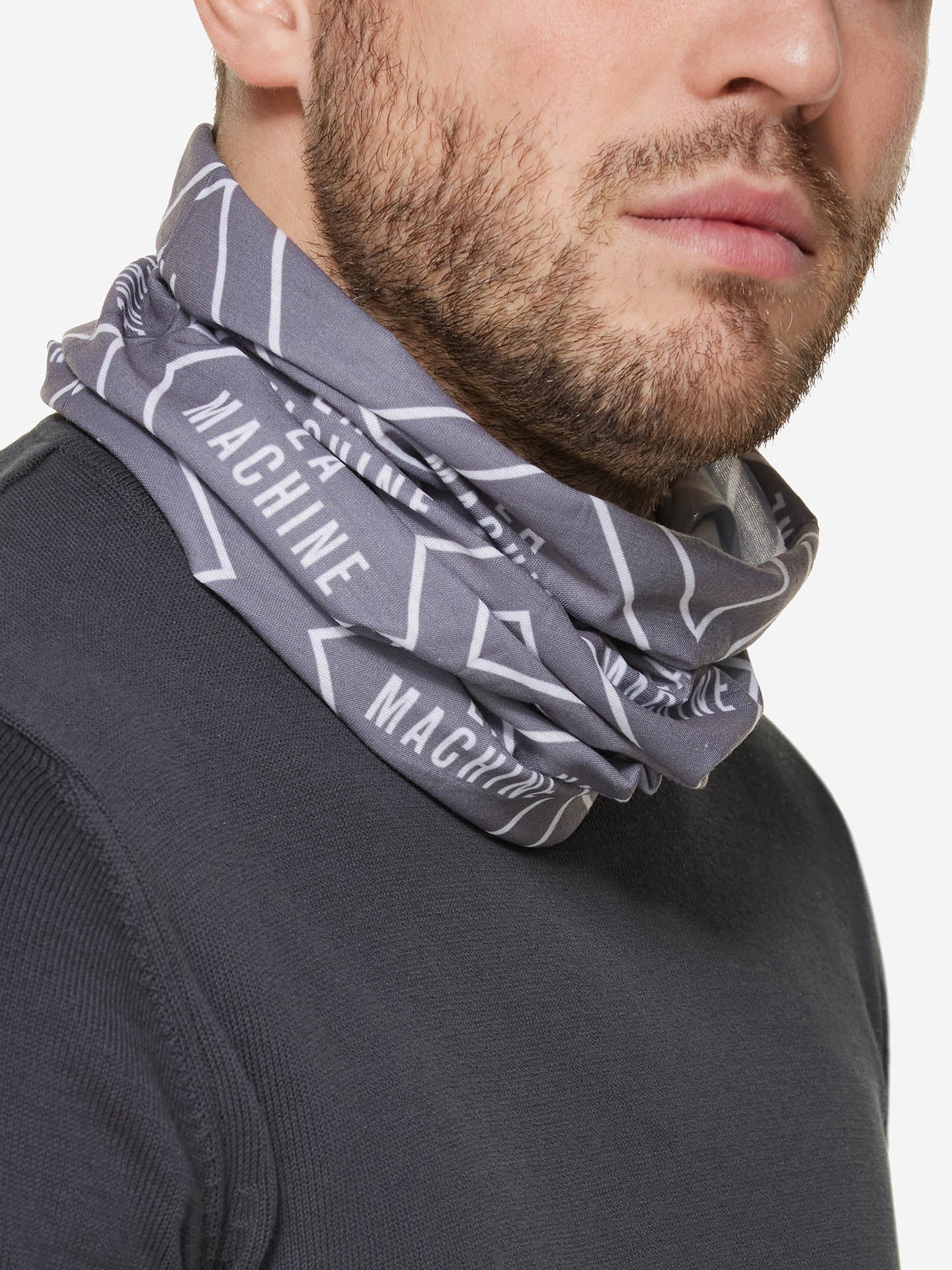 Close-up of a man wearing the La Machine Cycle Clubs La Machine Neck Warmer – Grey featuring white geometric lines and MACHINE text, paired with a dark textured shirt; only his lower face and neck are visible.