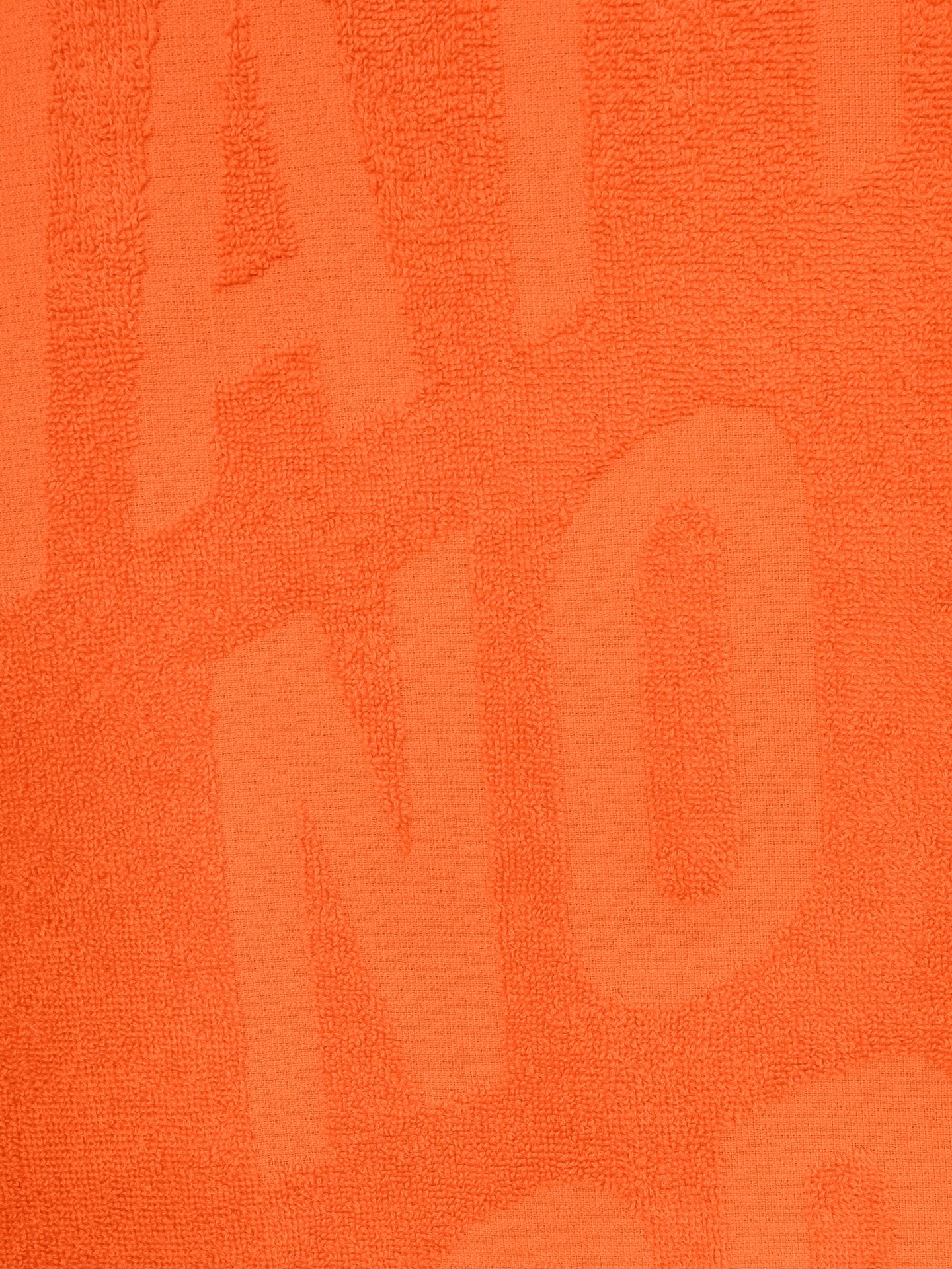 Close-up of textured orange fabric from the La Machine Cycle Club No Watts No Glory towel (60x80 cm), featuring large, raised letters for a bold, tactile pattern across the 100% cotton material.