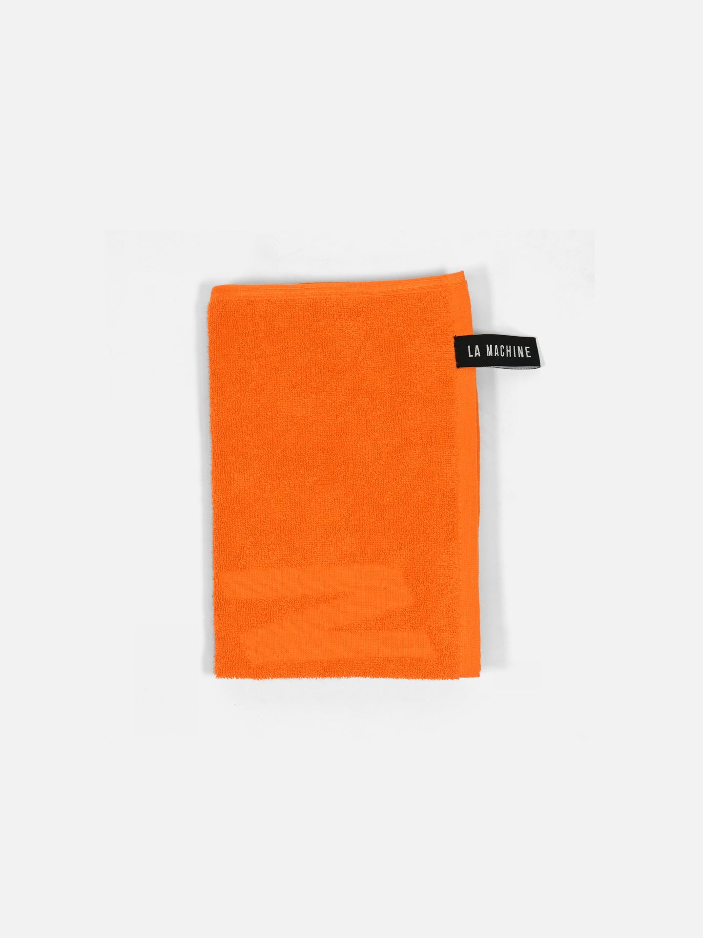 The No Watts No Glory - Towel (60x80 cm) by La Machine Cycle Club is an orange, rectangular 100% cotton gym towel with a black LA MACHINE label on one corner, shown on a plain white background.