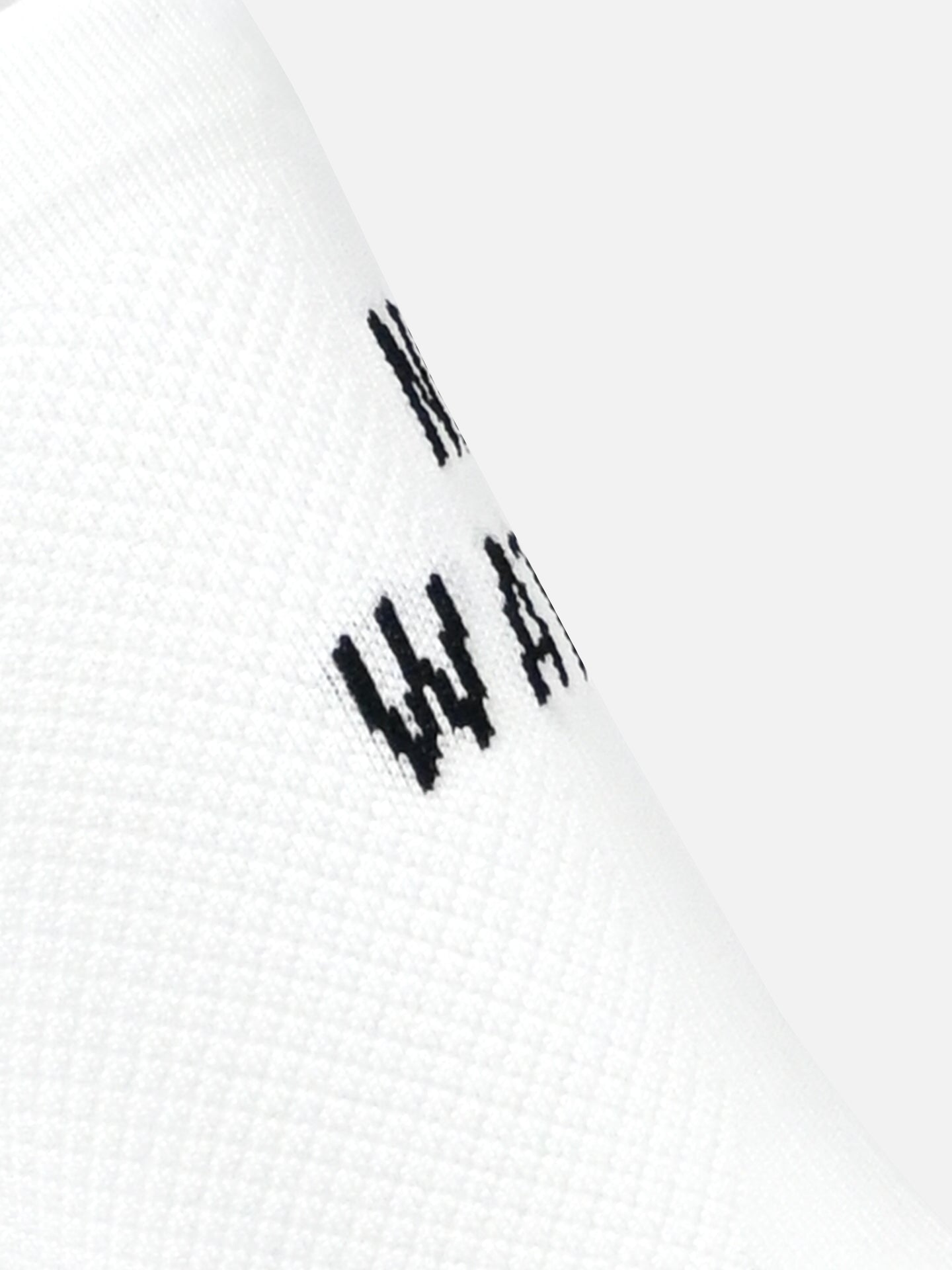 Close-up of textured white fabric from La Machine Cycle Clubs No Watts No Glory cycling socks, featuring a seamless toe and partially visible black W A letters. The background is plain light gray.