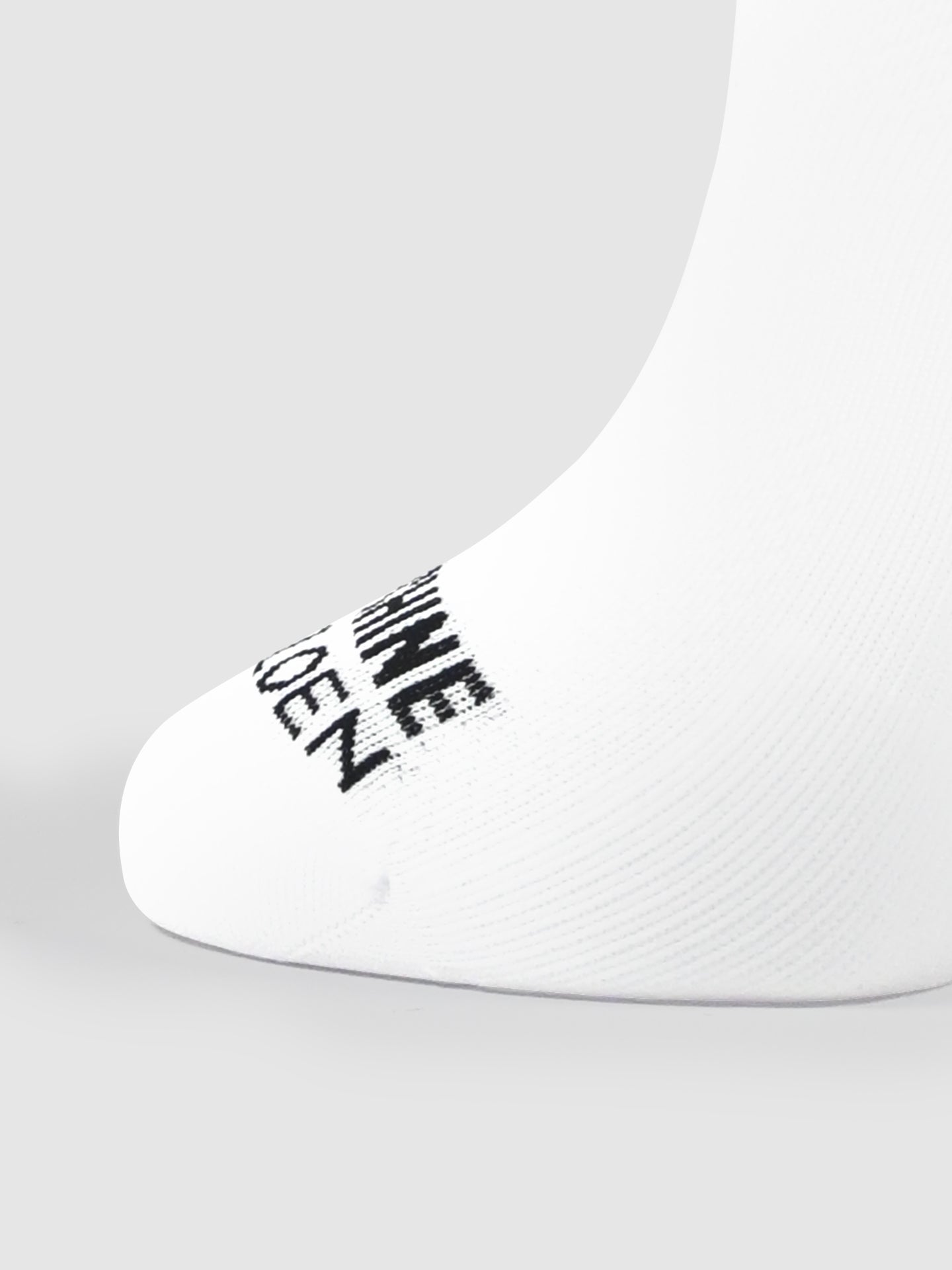 A close-up of La Machine Cycle Club’s Pedal Power - Cycling Socks in white, showing a seamless toe and black text near the toes, set against a plain light gray background.