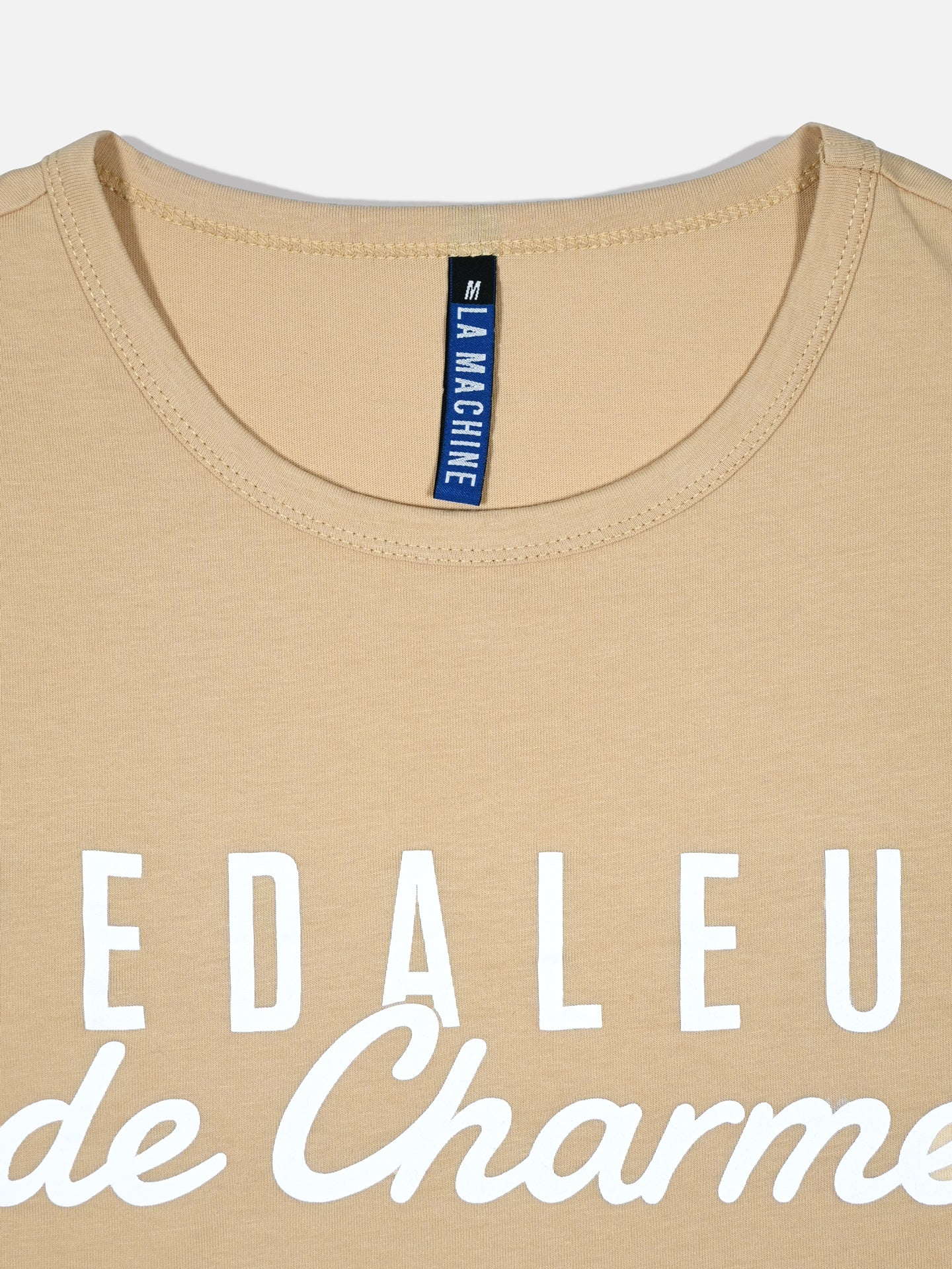 A sand-colored unisex cotton t-shirt from La Machine Cycle Club, featuring white printed text, a round neckline, and an M size tag—ideal for any Giro d’Italia fan. Product name: Pedaleur de Charme.
