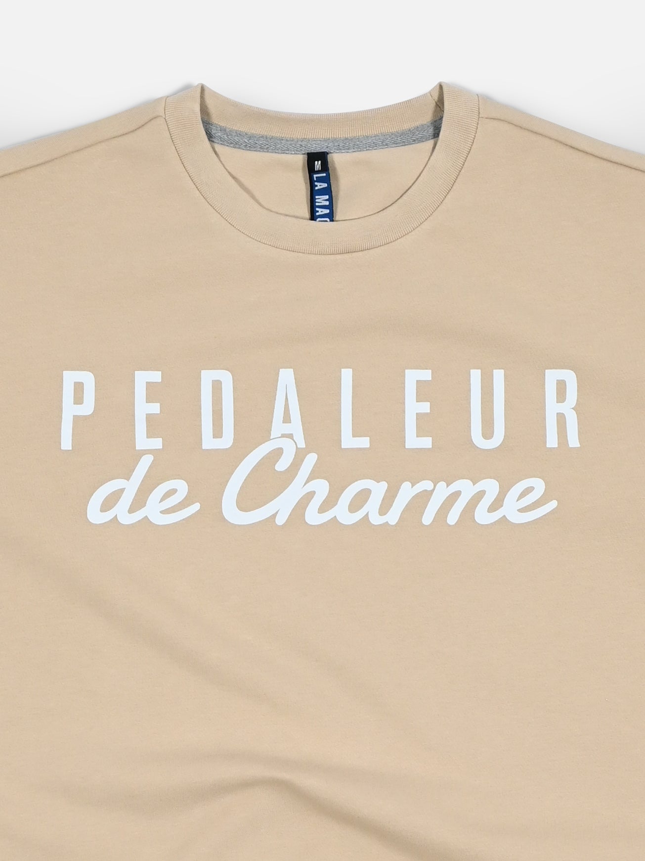 The Pedaleur de Charme - Sweatshirt - Sand by La Machine Cycle Club nods to Hugo Koblet’s style, with “PEDALEUR de Charme” in bold white, a round neckline, blue collar tag, and Giro d’Italia-inspired design.