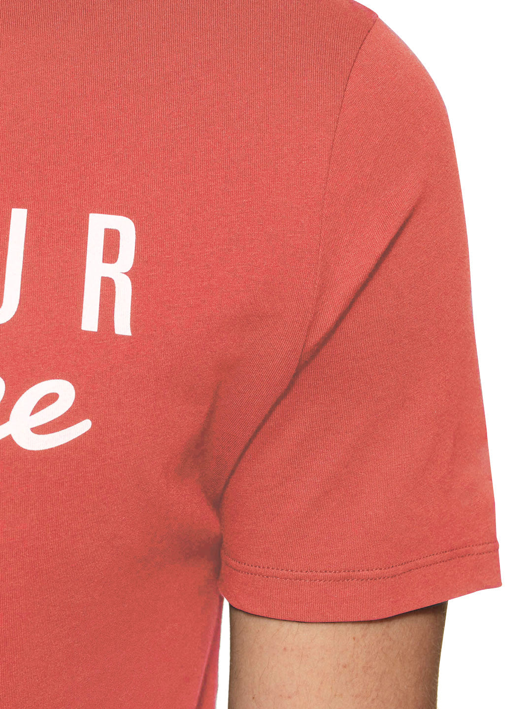 Close-up of a person wearing the Pedaleur de Charme - T-shirt in coral by La Machine Cycle Club, made from premium cotton with partial white print. Only the upper torso and right arm are shown against a plain white background.