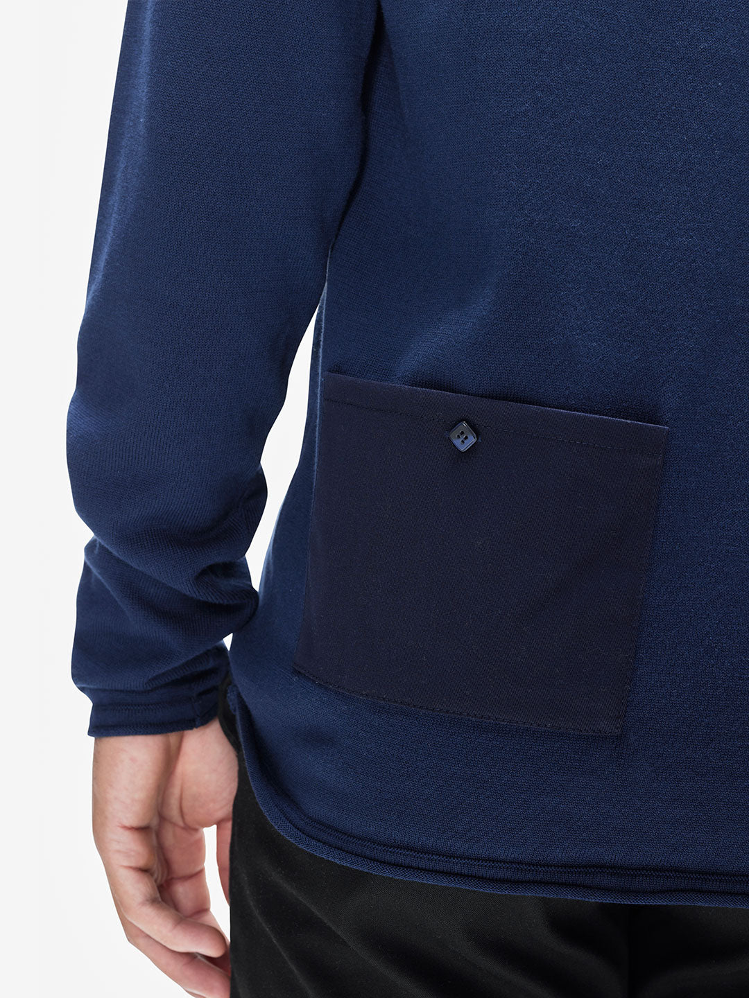 A person wears the La Machine Cycle Club Premium Knitted Pullover, a mens long-sleeved navy top featuring a matching square pocket with a button on the lower back. Only part of their arm and hand appears against a plain background.