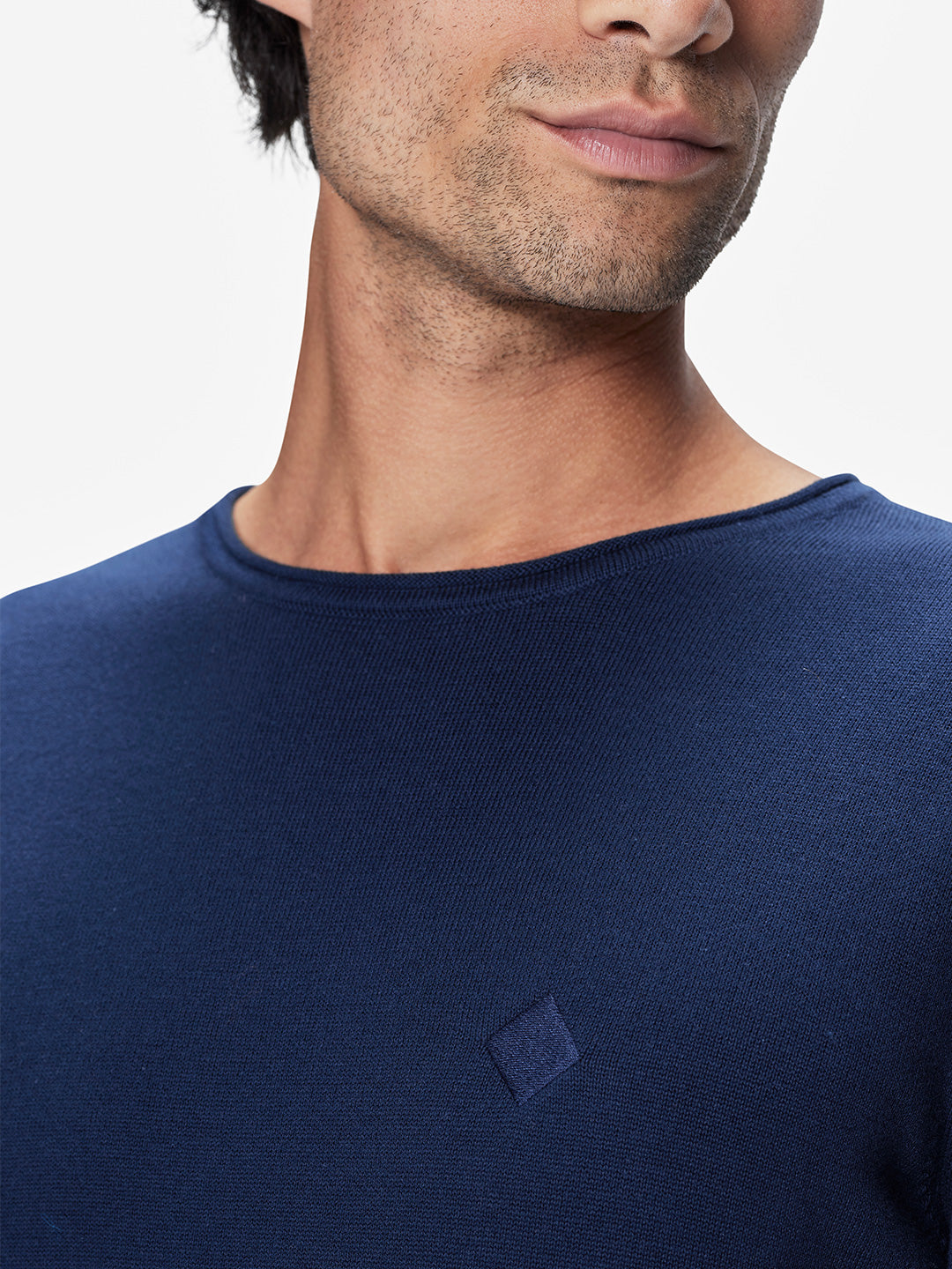 Close-up of a person wearing the La Machine Cycle Club Premium Knitted Pullover, featuring a blue crewneck design with a small square chest logo; photo shows lower face, neck, and upper torso against a plain background.