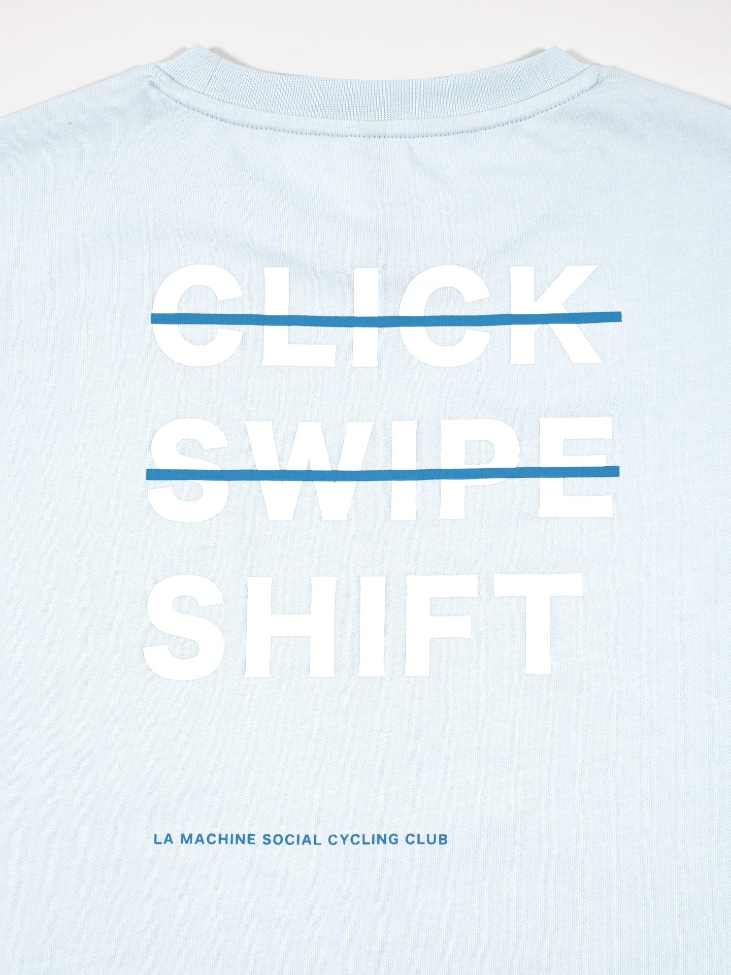 The La Machine Cycle Club Social Cycling Club - Loose Fit T-shirt is a light blue heavy cotton tee with CLICK, SWIPE, SHIFT in bold white letters crossed by a blue line and “Social Cycling Club” below, plus a standout large back print.