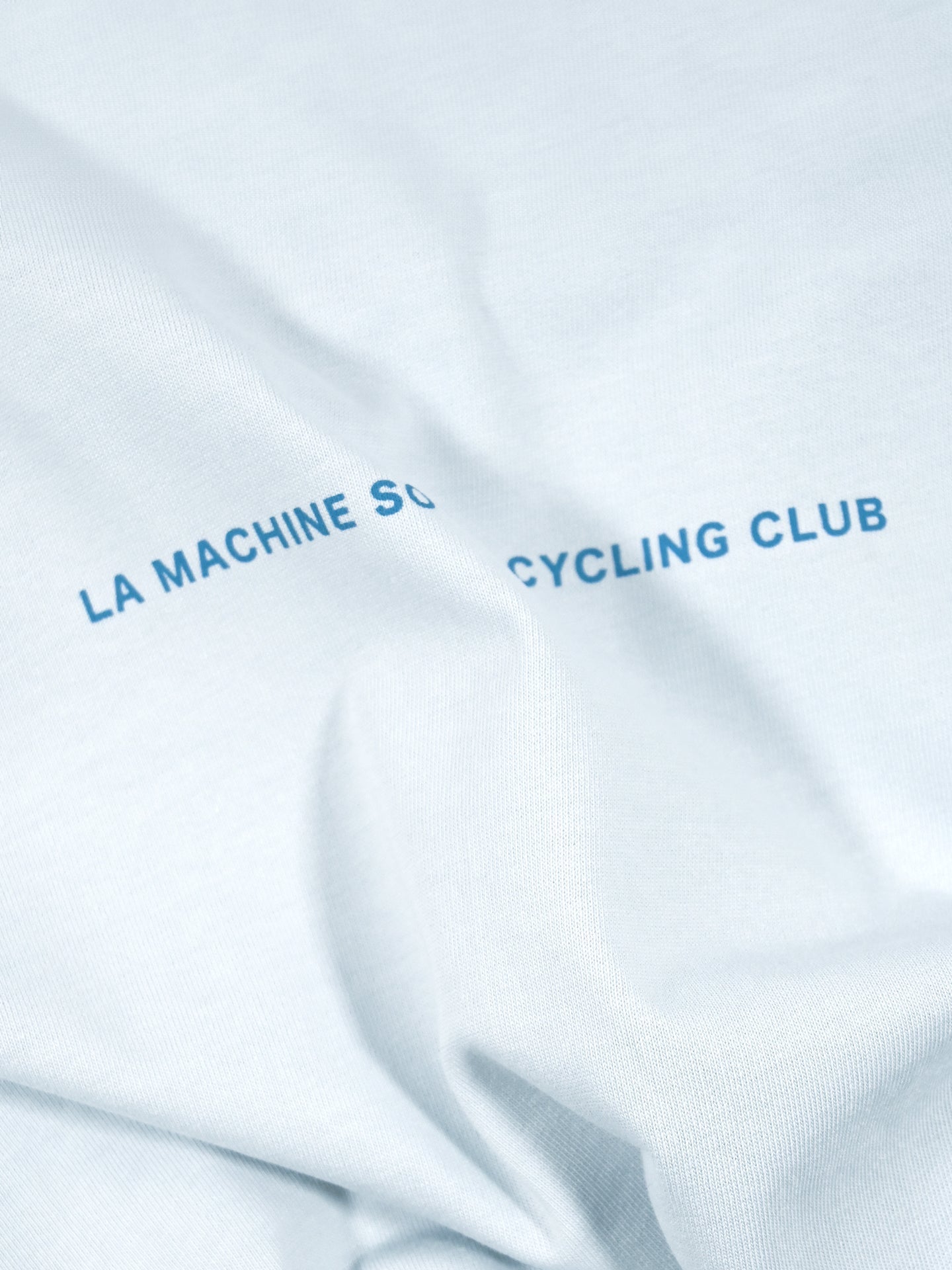 This light blue, heavy cotton Social Cycling Club Loose Fit T-shirt by La Machine Cycle Club features a slightly wrinkled texture and a large back print: “LA MACHINE S... CYCLING CLUB,” partially obscured by fabric folds.