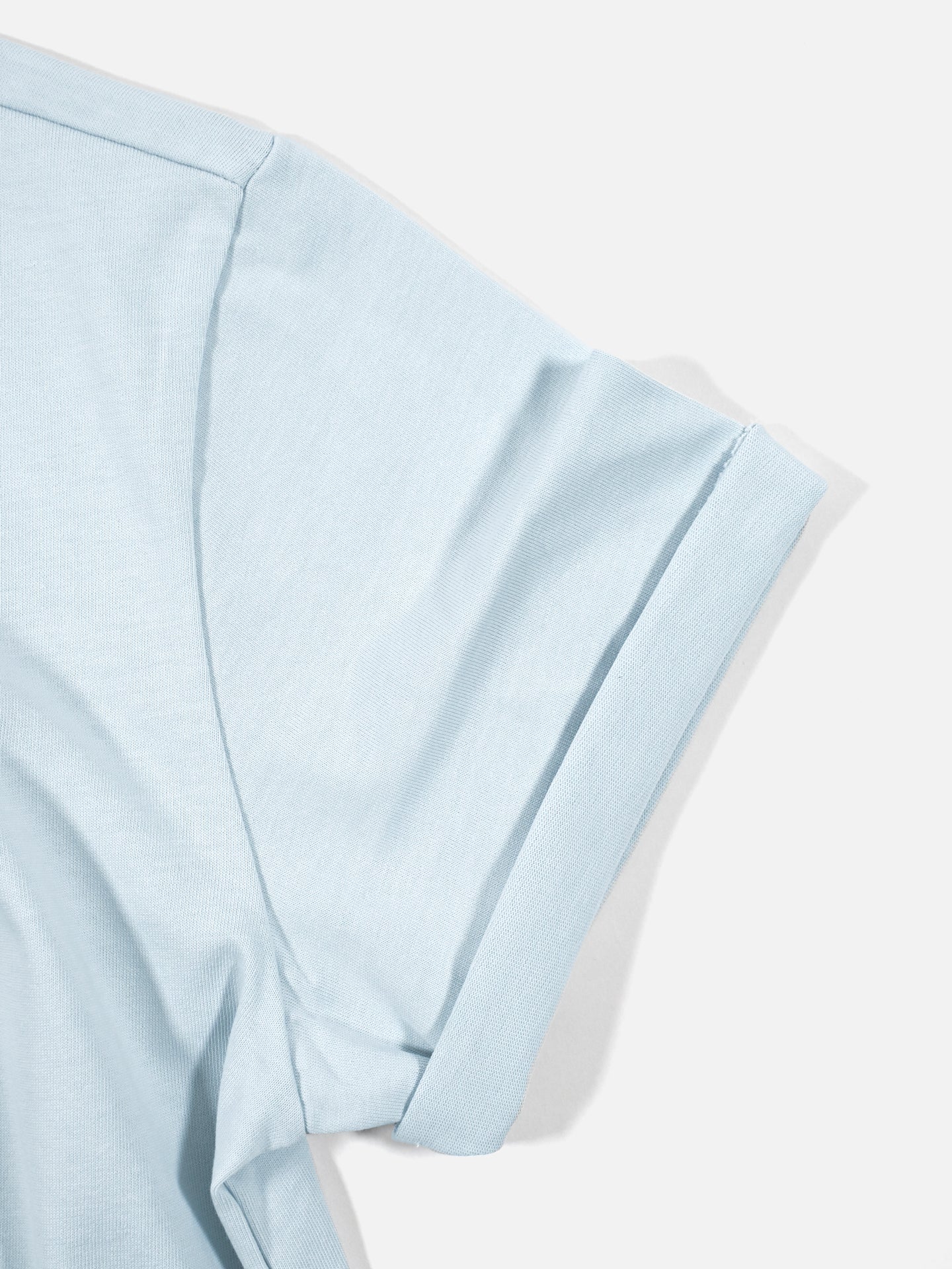 Close-up of the upper sleeve and shoulder of the La Machine Cycle Club Social Cycling Club Loose Fit T-shirt in light blue, made from heavy cotton with soft, smooth fabric and visible seam stitching, laid flat on a white background.