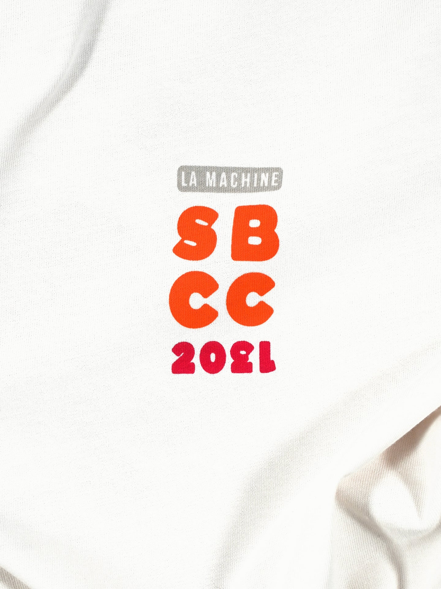 The Sticky Bottles - Loose Fit T-shirt from La Machine Cycle Club is made of heavy white cotton and features a bold back print: LA MACHINE (gray), SBCC (orange), and 2021 (red) in playful, standout fonts.