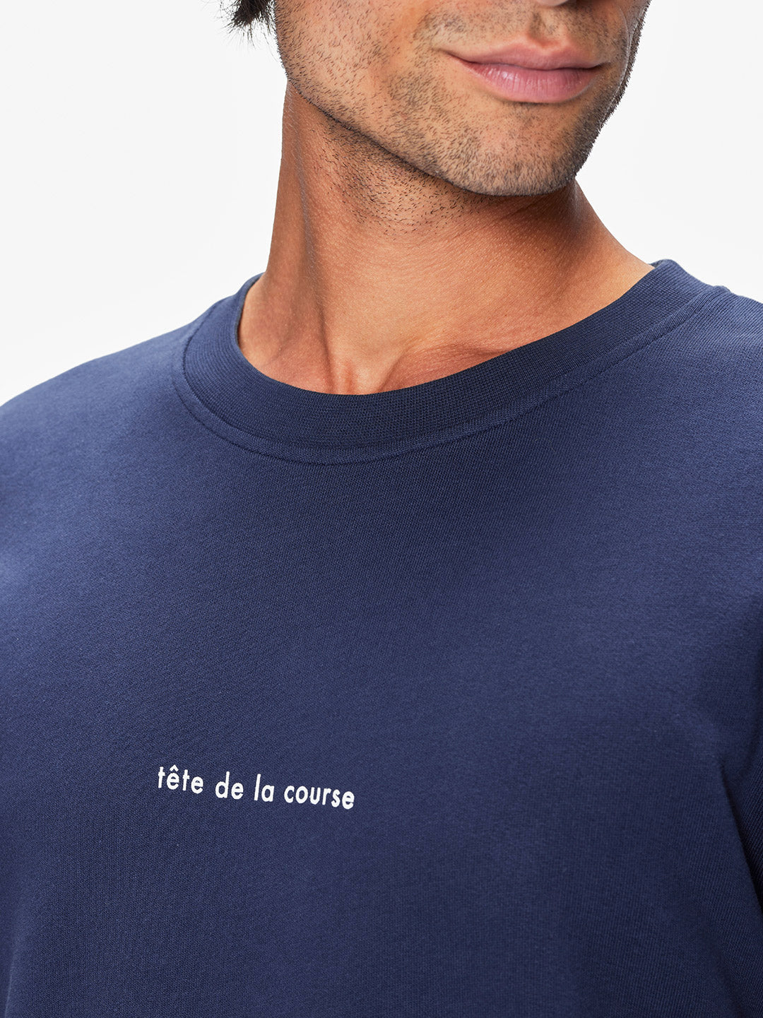 A man wears La Machine Cycle Club’s Tête de la Course navy cycling-style men’s sweatshirt with “tête de la course” in white on the chest. Only the lower face and upper torso are visible. Made from 100% cotton for comfort.