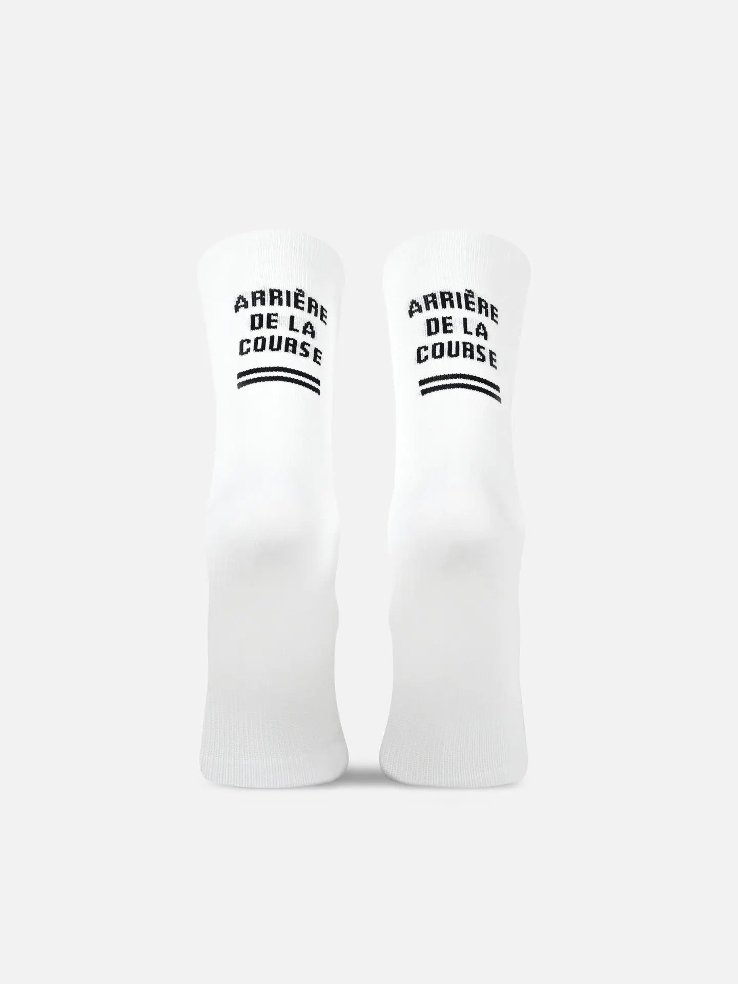 Two white Tête de la Course cycling socks by La Machine Cycle Club stand upright, each featuring ARRIÈRE DE LA COURSE in black above two horizontal lines on the front. Designed for optimum elastic comfort. Background is plain white.
