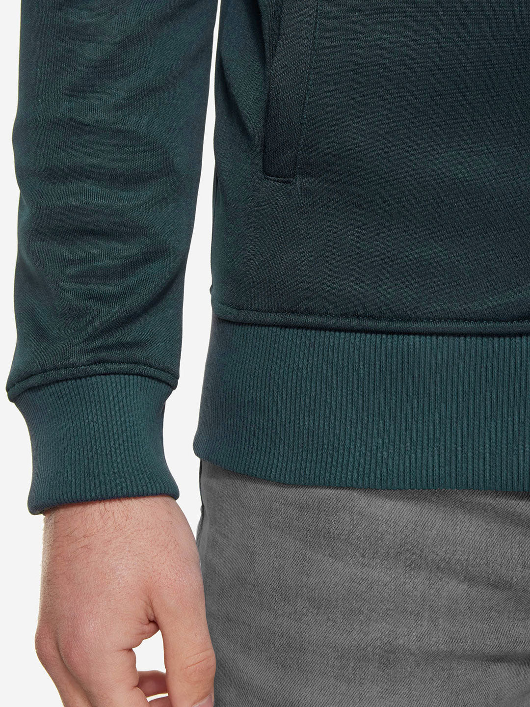 A close-up of a person in the La Machine Cycle Club Food of Champions - Track Jacket in Atlantic Deep, featuring ribbed cuffs and hem, paired with gray pants. The tailored fit gives a sleek edge to this casual look.