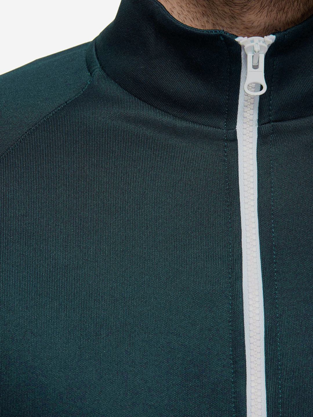 Close-up of the La Machine Cycle Club “Food of Champions - Track Jacket - Atlantic Deep” in dark green, tailored fit, and white zipper, highlighting the collar and upper chest. The lower face and neck are partially visible.