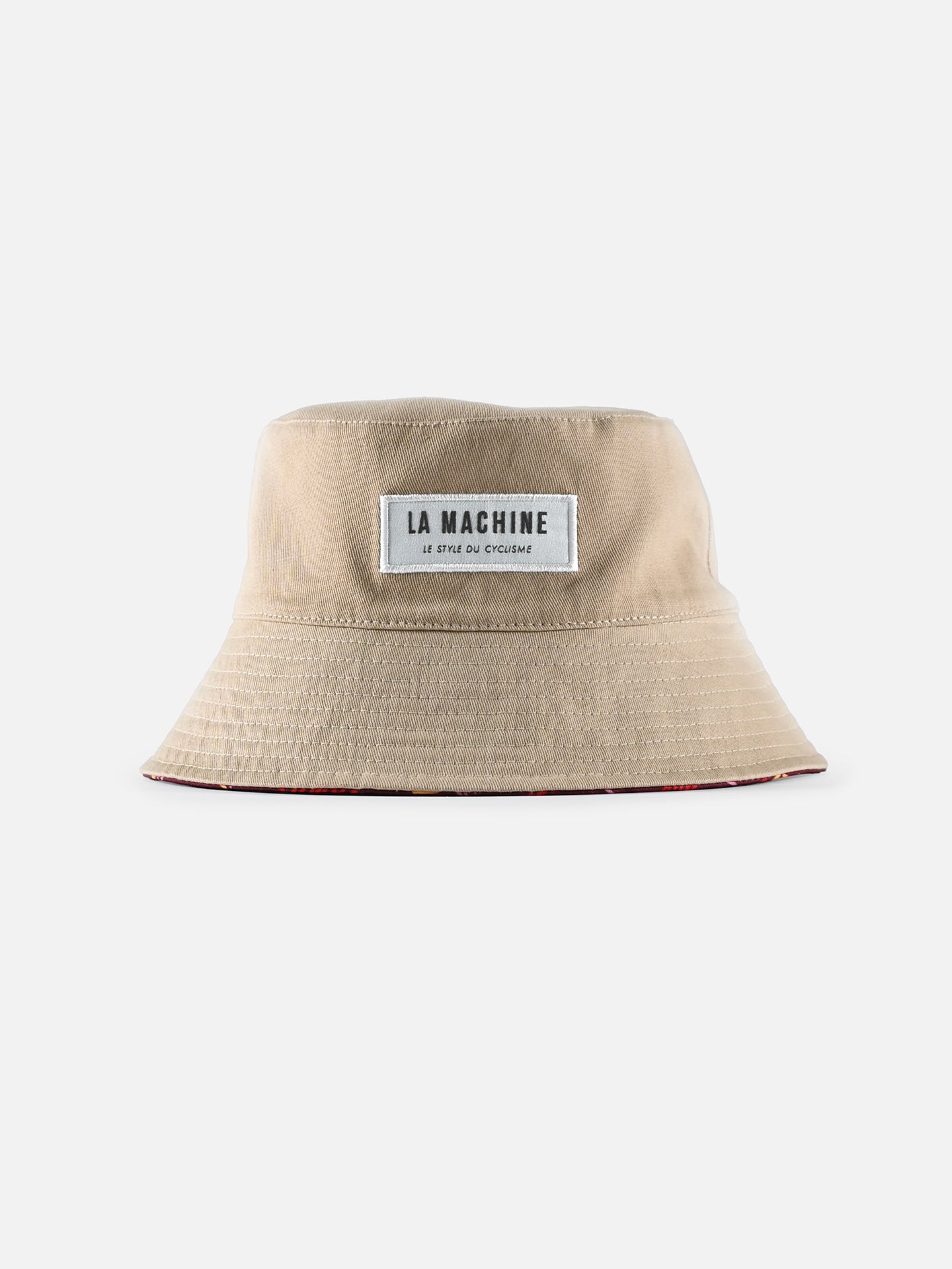 The La Machine - Reversible Bucket Hat by La Machine Cycle Club is beige with a wide brim and features a white front patch reading LA MACHINE. Classic Grand Tour cycling style, displayed on a plain white background.