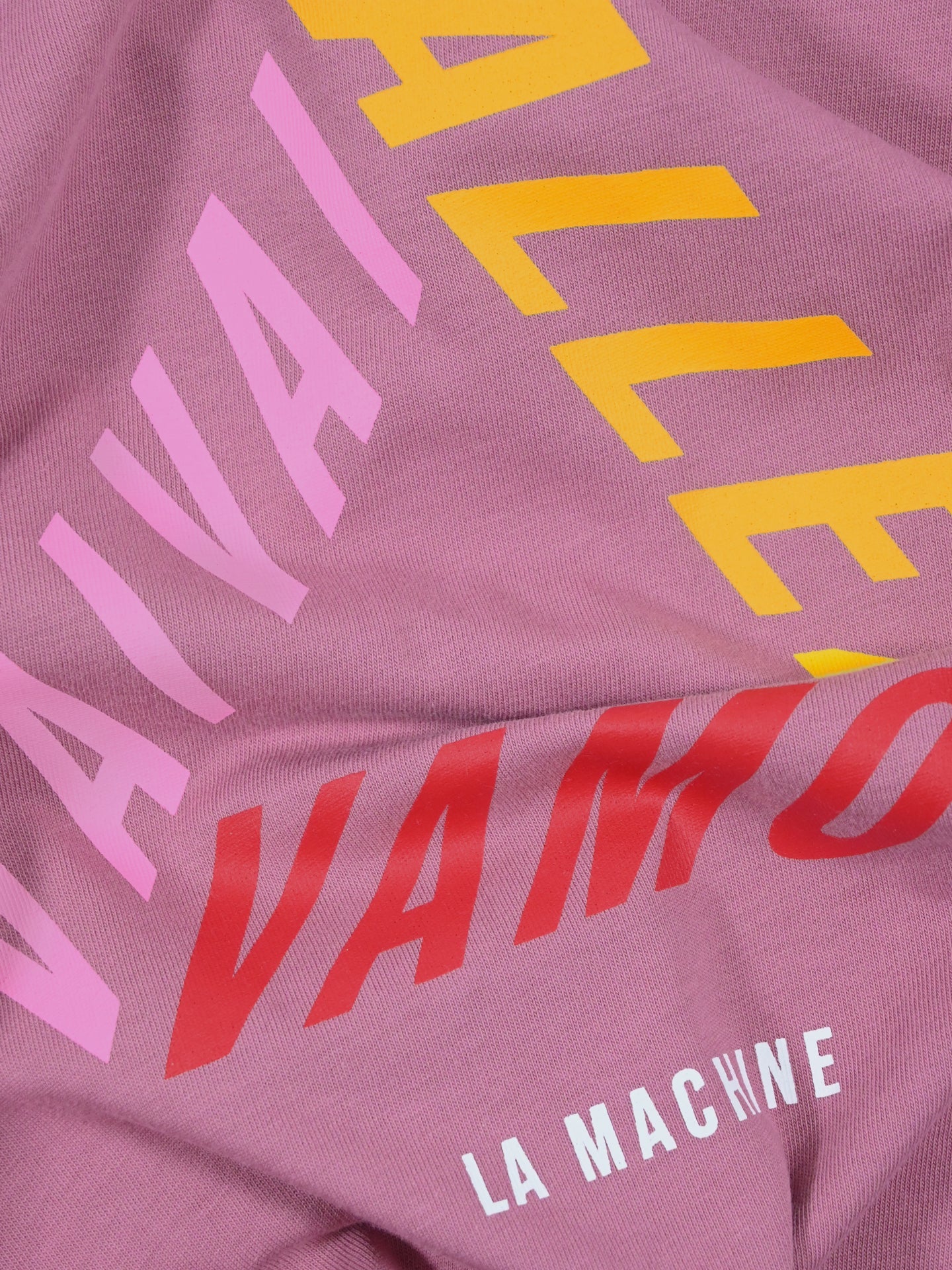 Close-up of the unisex Vai Allez Vamos - Loose Fit T-shirt from La Machine Cycle Club, featuring bold “VAI VAI”, “ALLEZ”, and “VAMOS” text in pink, yellow, and red, with LA MACHINE in white at the bottom.